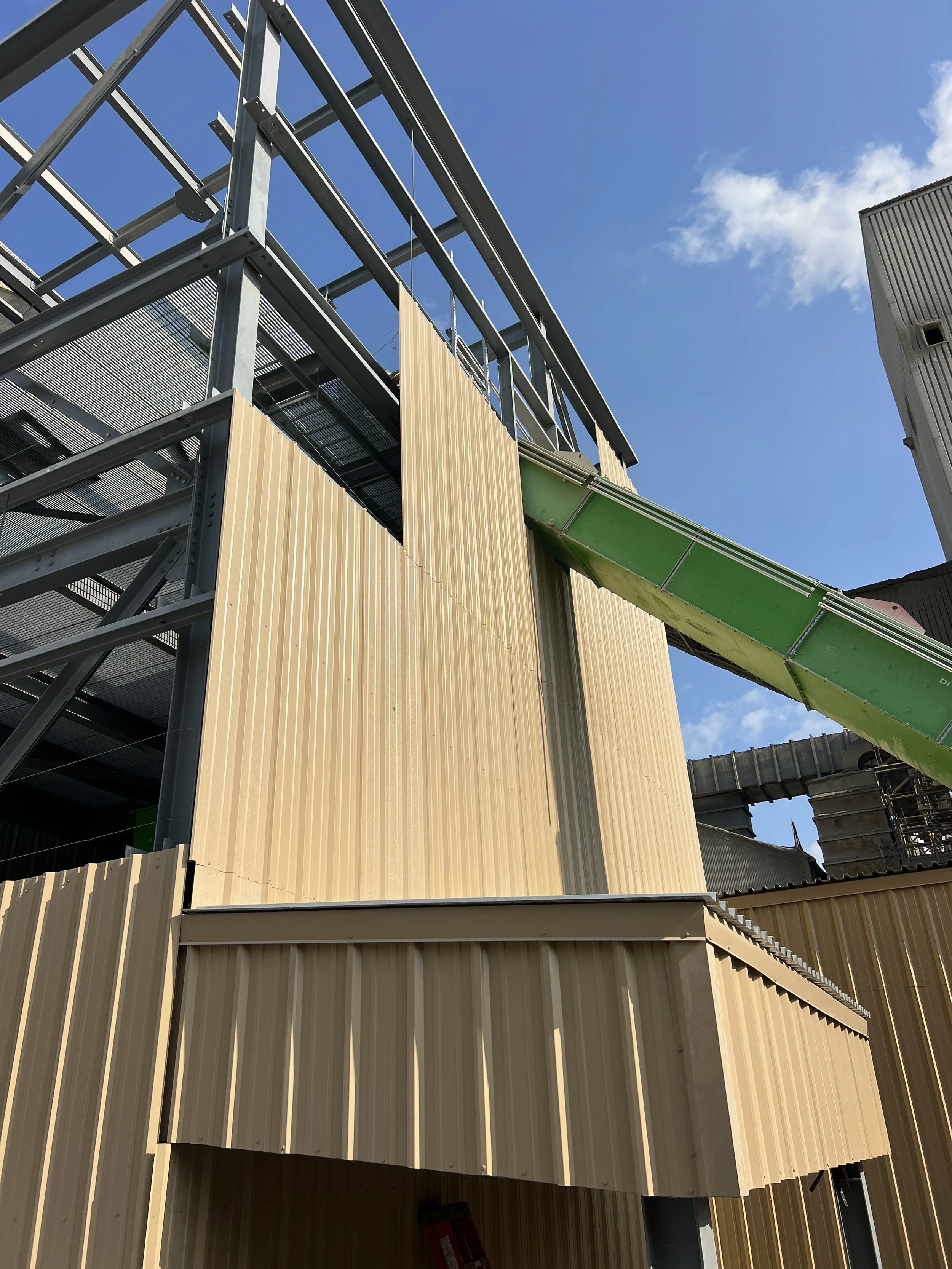 Construction site with metal framework and beige exterior panels, green slide, clear blue sky with some clouds.