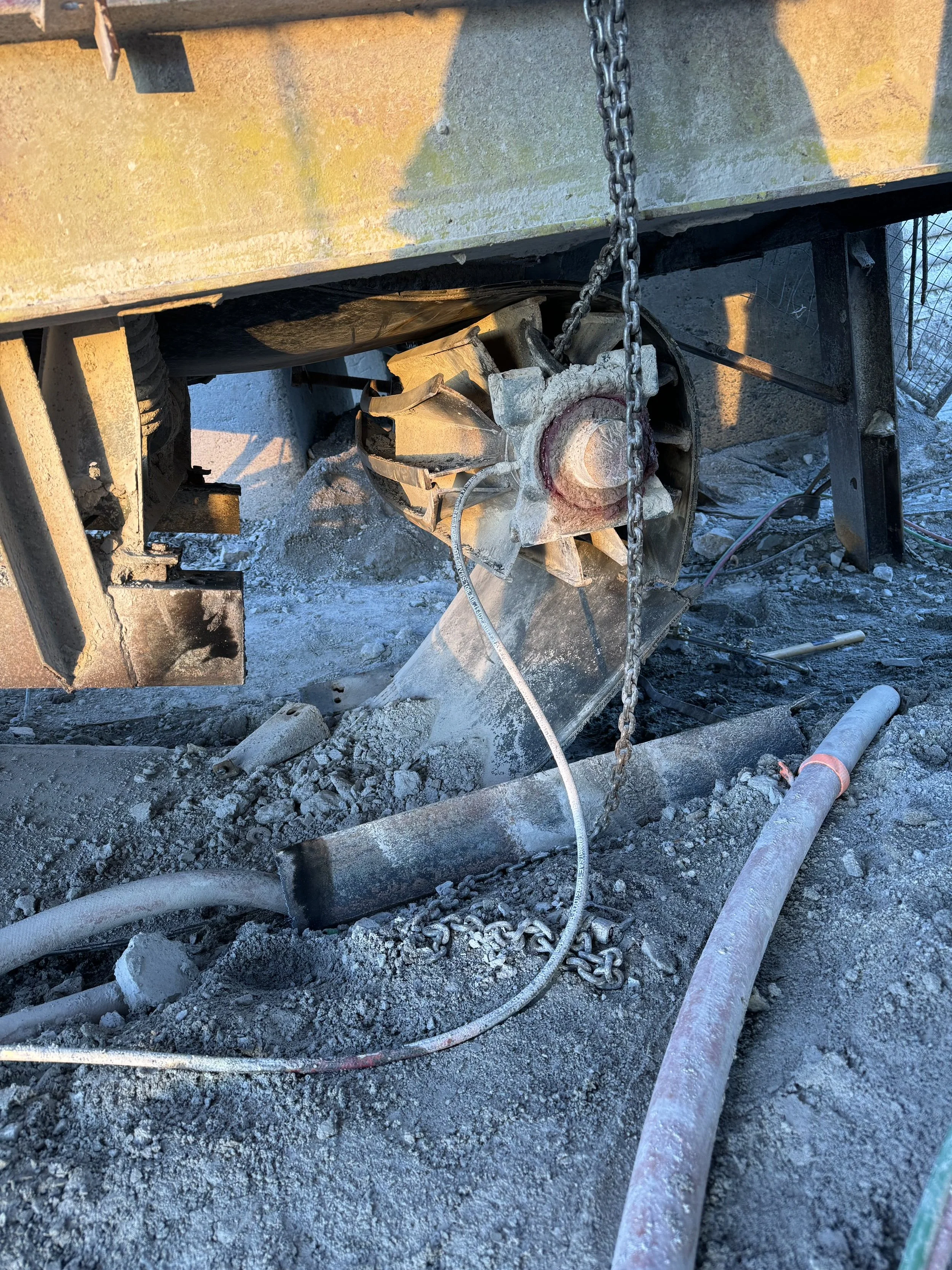 Construction site with debris, chains, and pipes on a dirt ground.