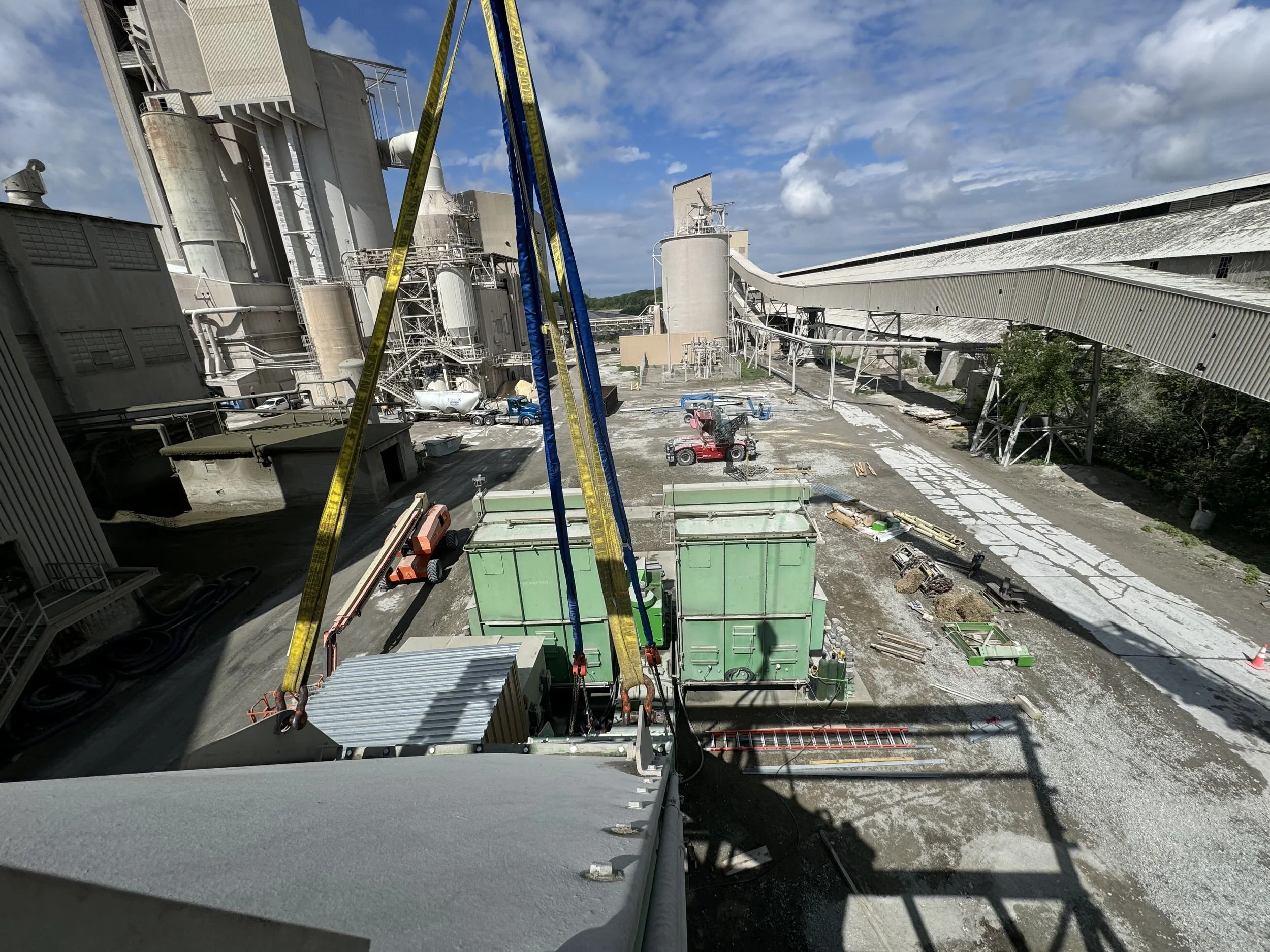 Construction site with large industrial buildings, scaffolding, vehicles, and construction equipment under a partly cloudy sky.