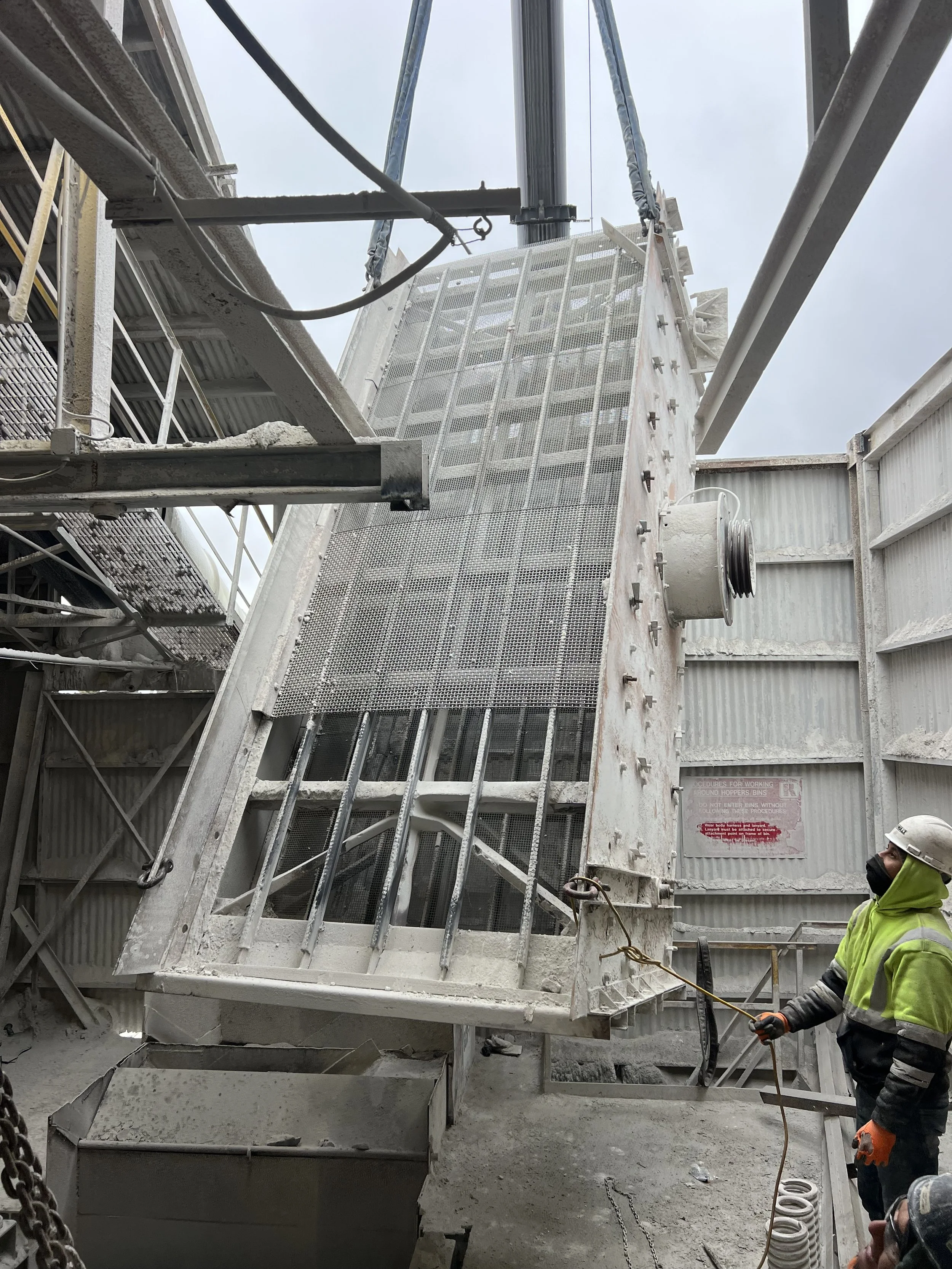 Construction site with large metal machinery, workers in safety gear, and a worker holding a tool.