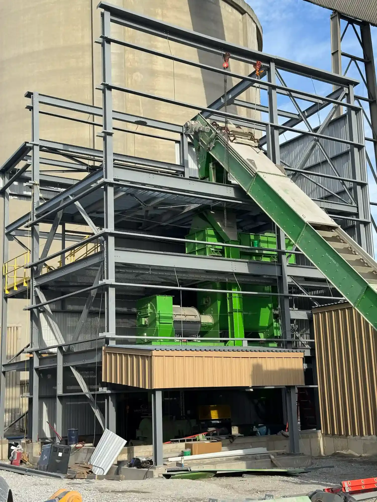 Steel-framed plant under construction with green conveyor and processing machinery