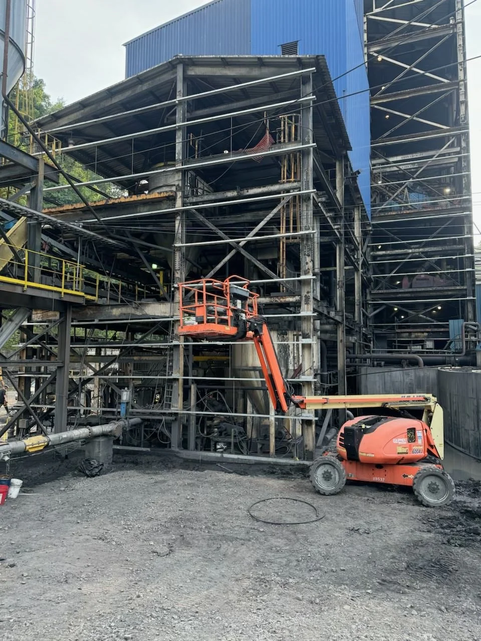 Construction site with a fire-resistant orange lift machine and steel framework of a building under construction.