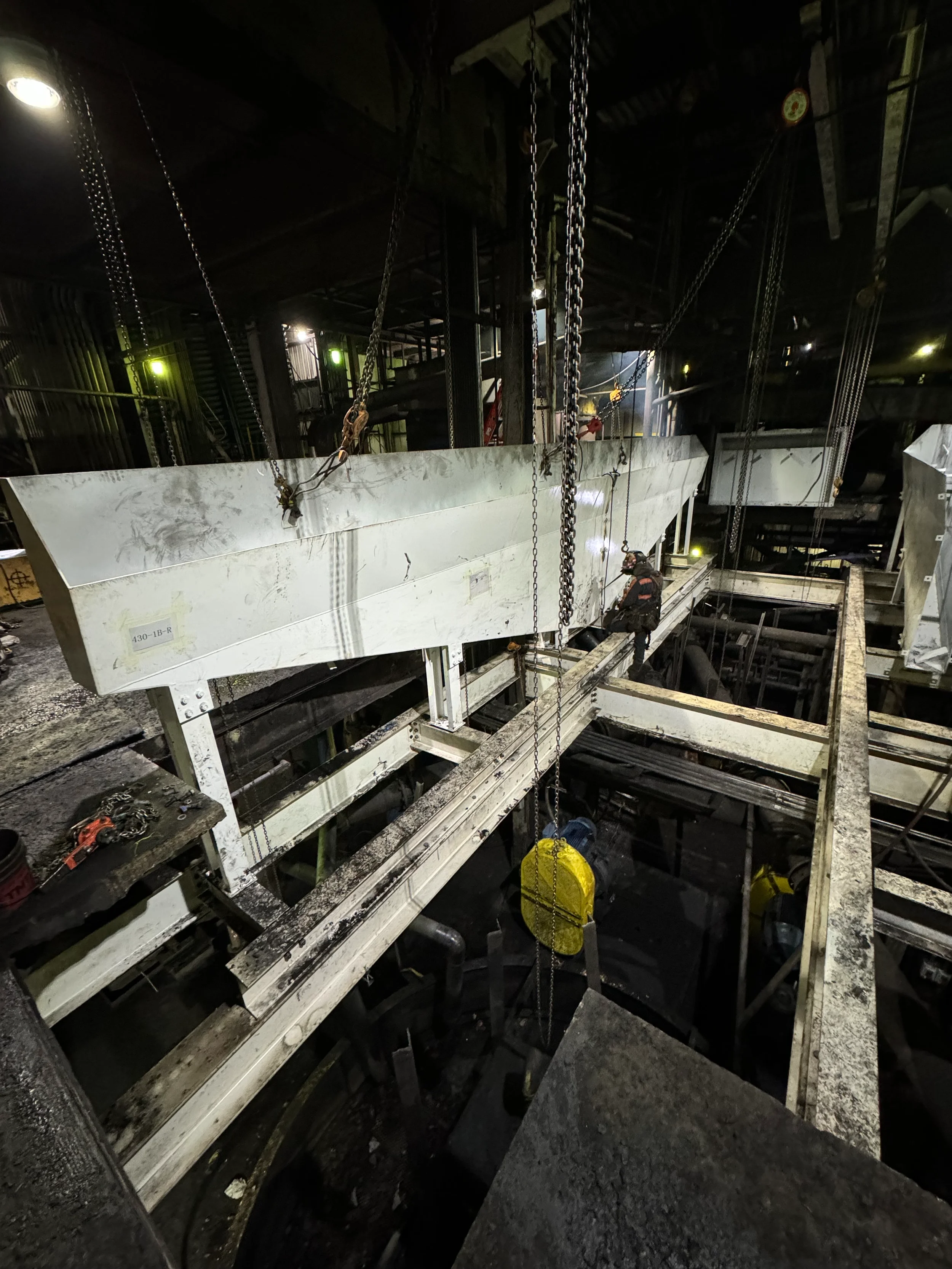 Workers in safety gear working inside an industrial facility with chains, metal structures, and machinery.