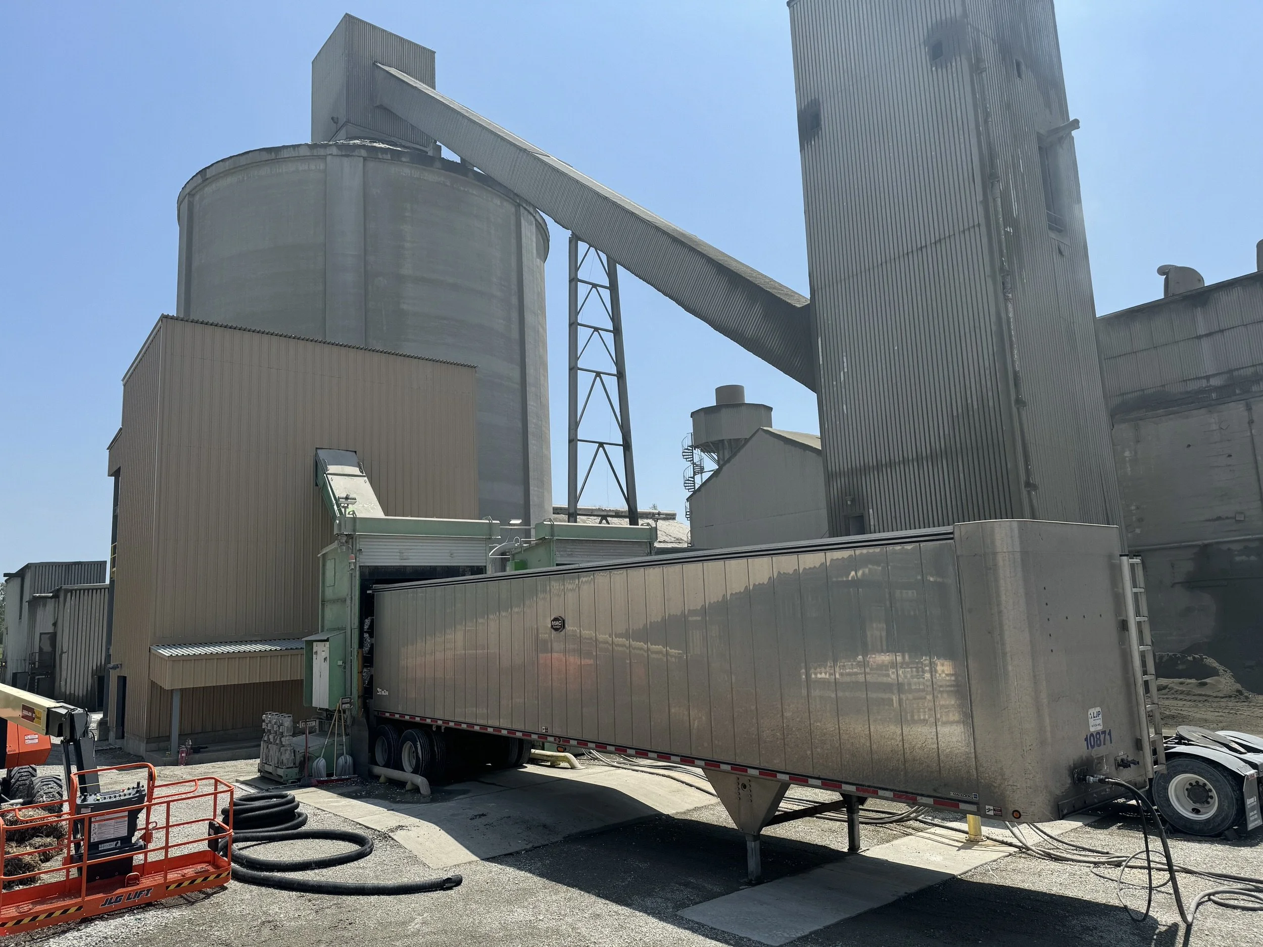 Industrial building with silos, conveyor, and construction equipment, under a clear blue sky.