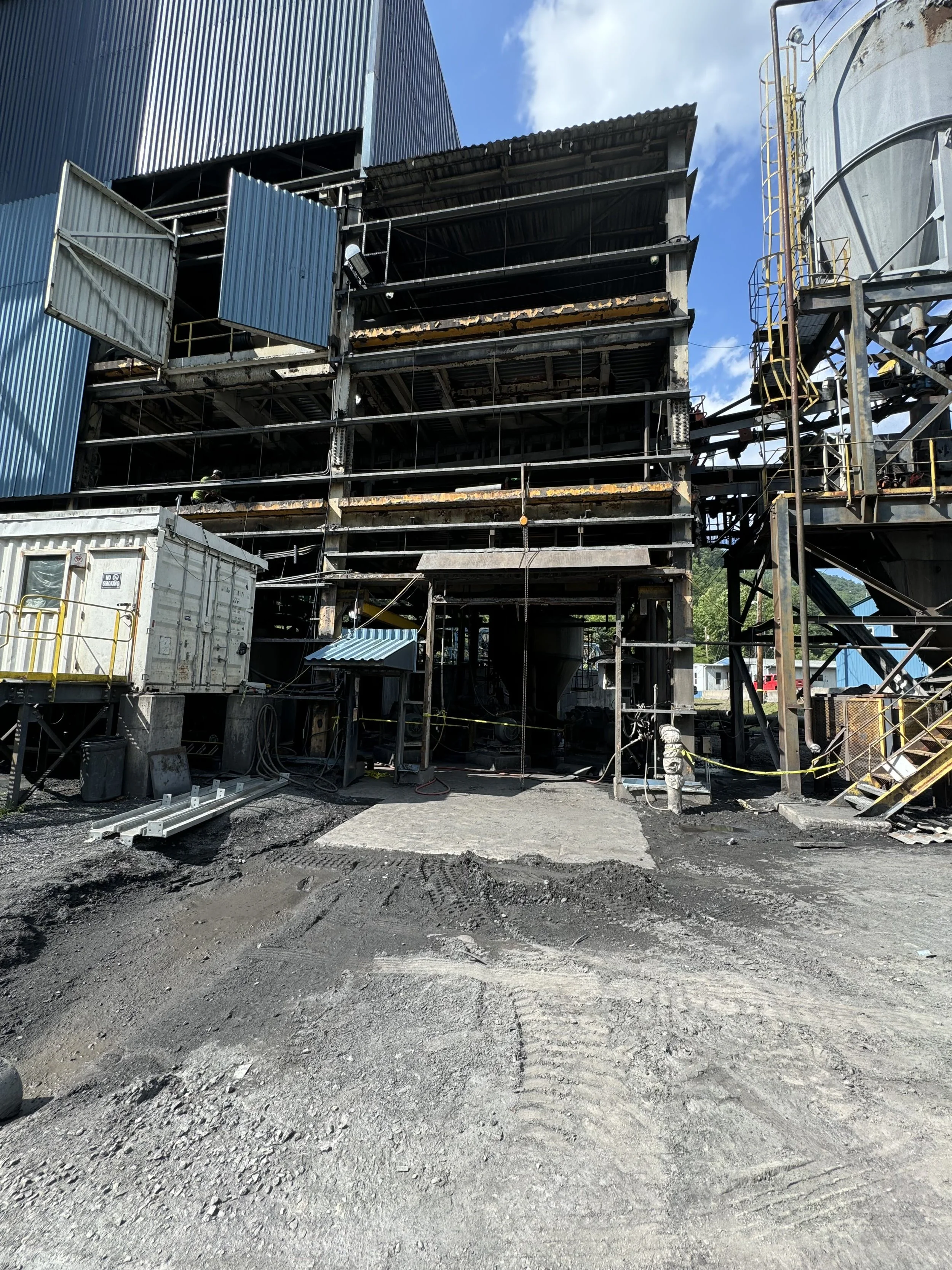 Construction site with unfinished building, construction materials, and equipment, with a gravel ground and a blue sky.