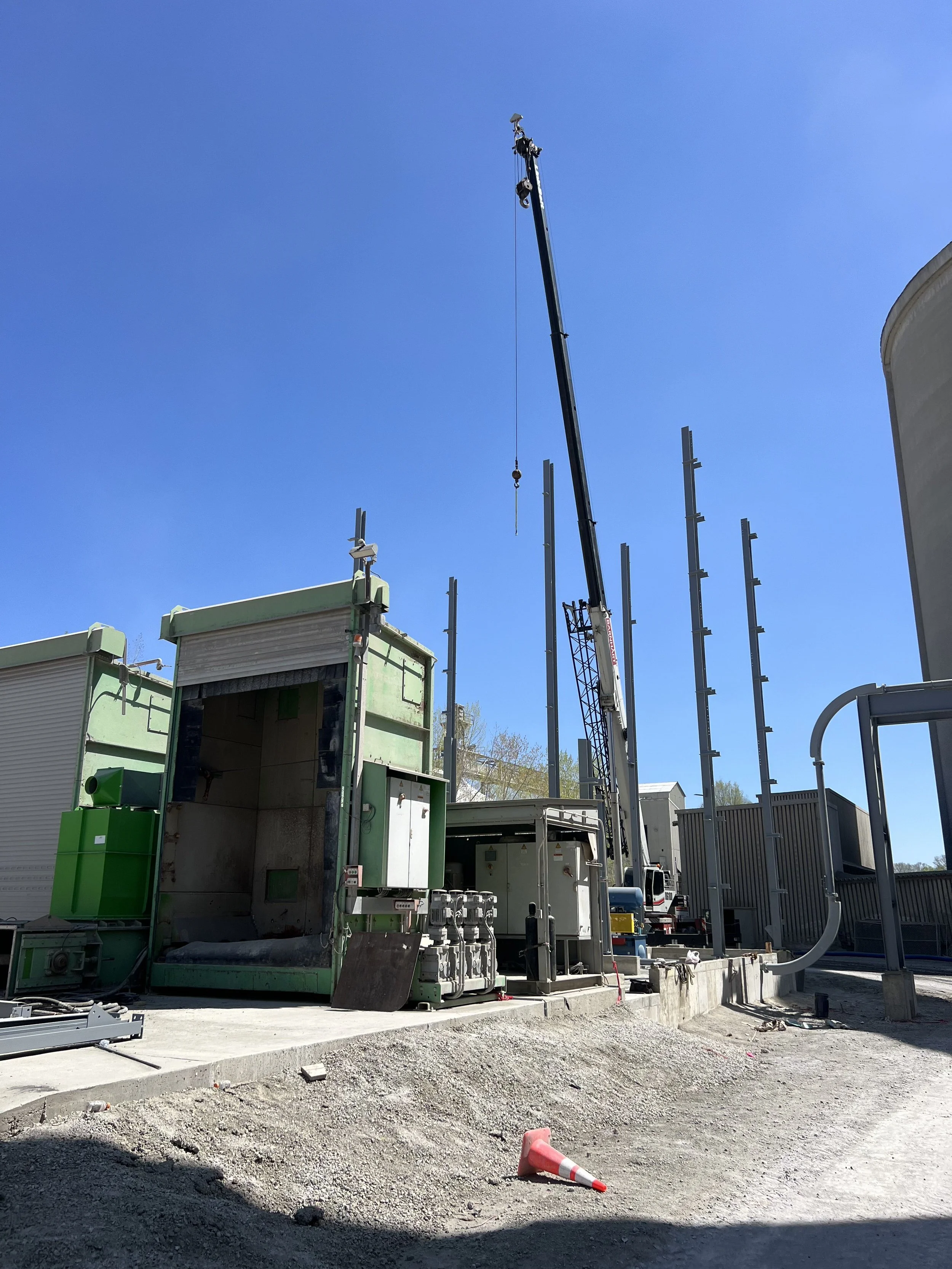 Construction site with machinery, a crane, and partial building structure under a clear blue sky.