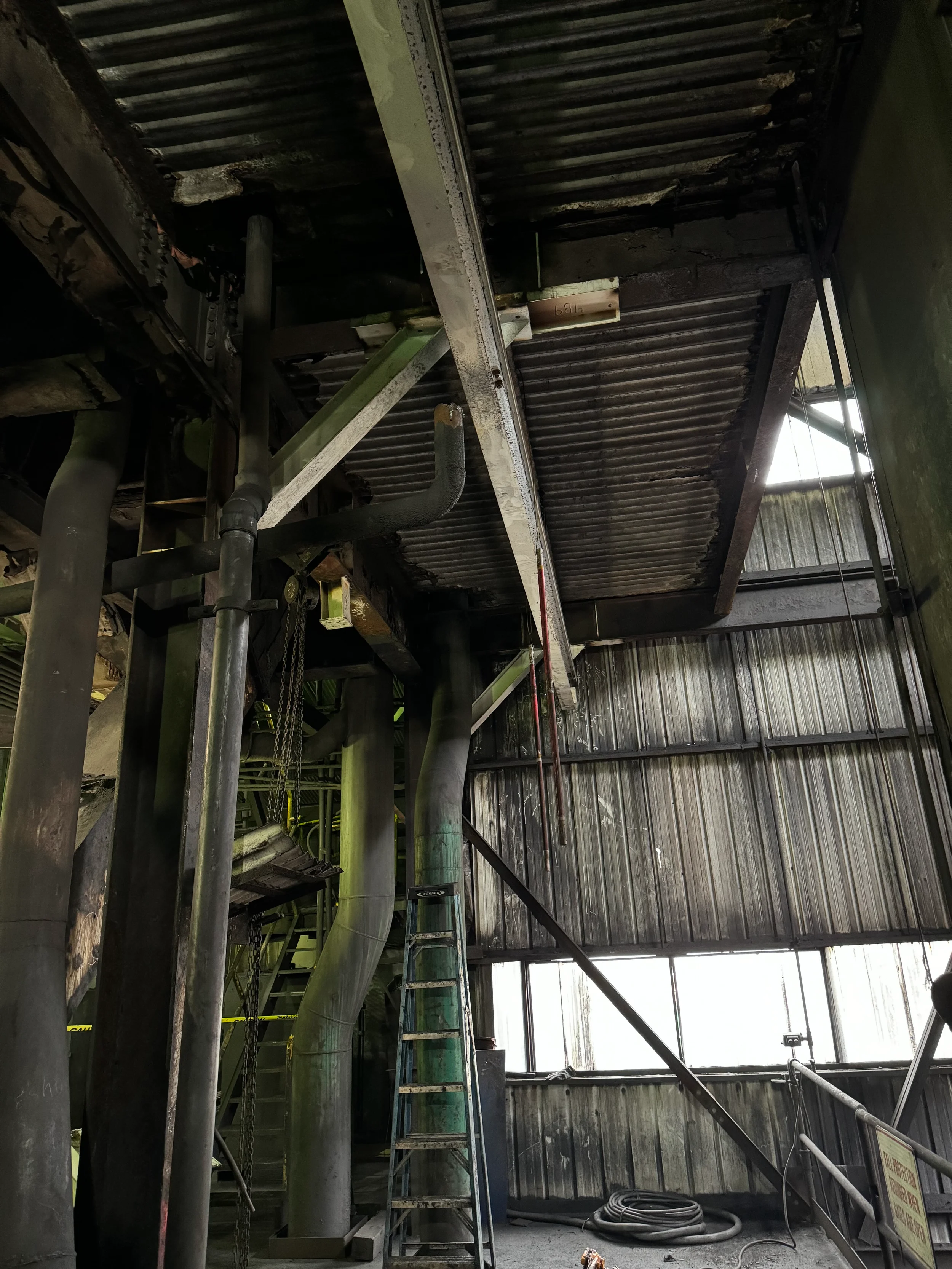 Construction site with scaffolding, pipes, and a ladder inside a building with metal siding and a partially open roof.
