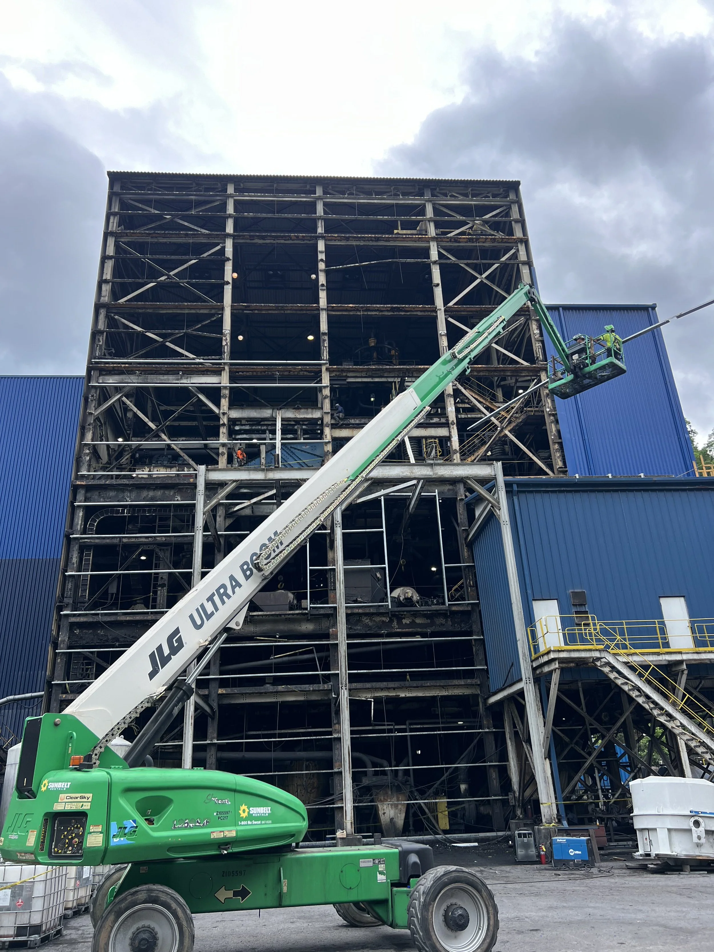 Construction site with a partially demolished building with exposed steel framework and a green boom lift with workers.
