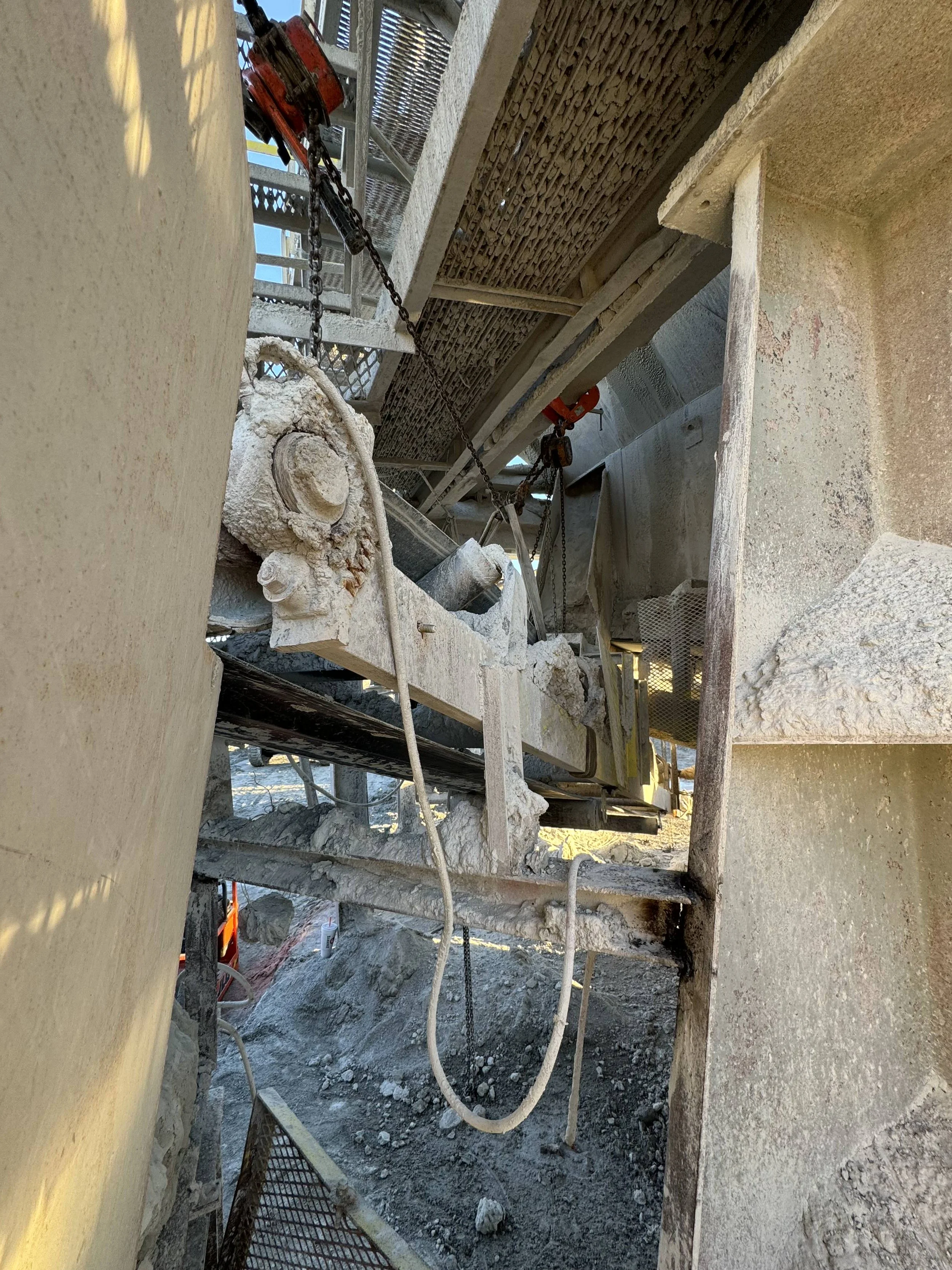 Construction site with concrete and metal framework, chains, and equipment, likely for building or repair work.