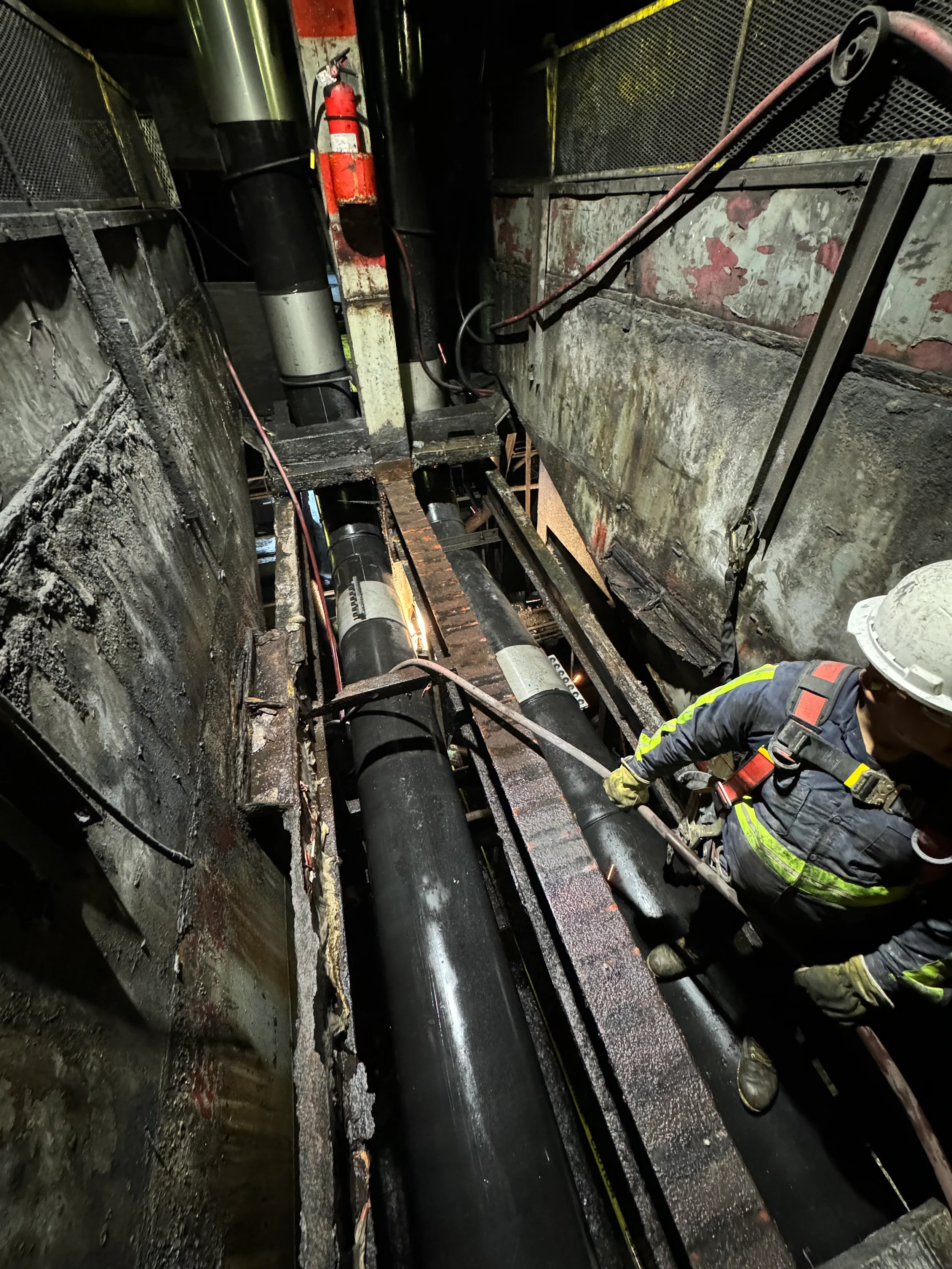 A firefighter inspecting a large underground pipe fault or leak in an industrial or utility tunnel, with walls showing damage and soot.