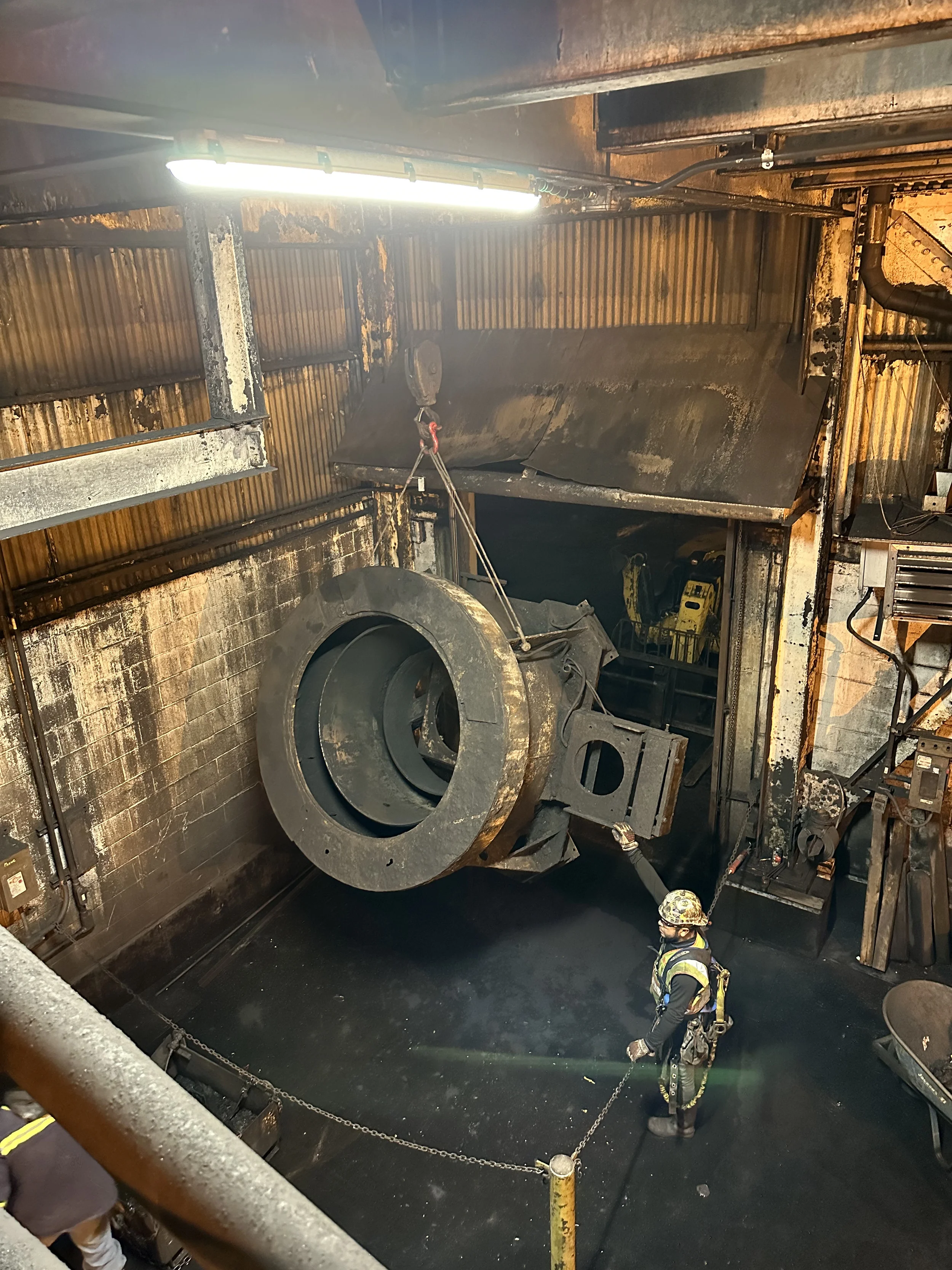 Firefighters inspecting the aftermath of a fire inside a large industrial or mechanical facility, with burnt industrial equipment and charred surroundings.