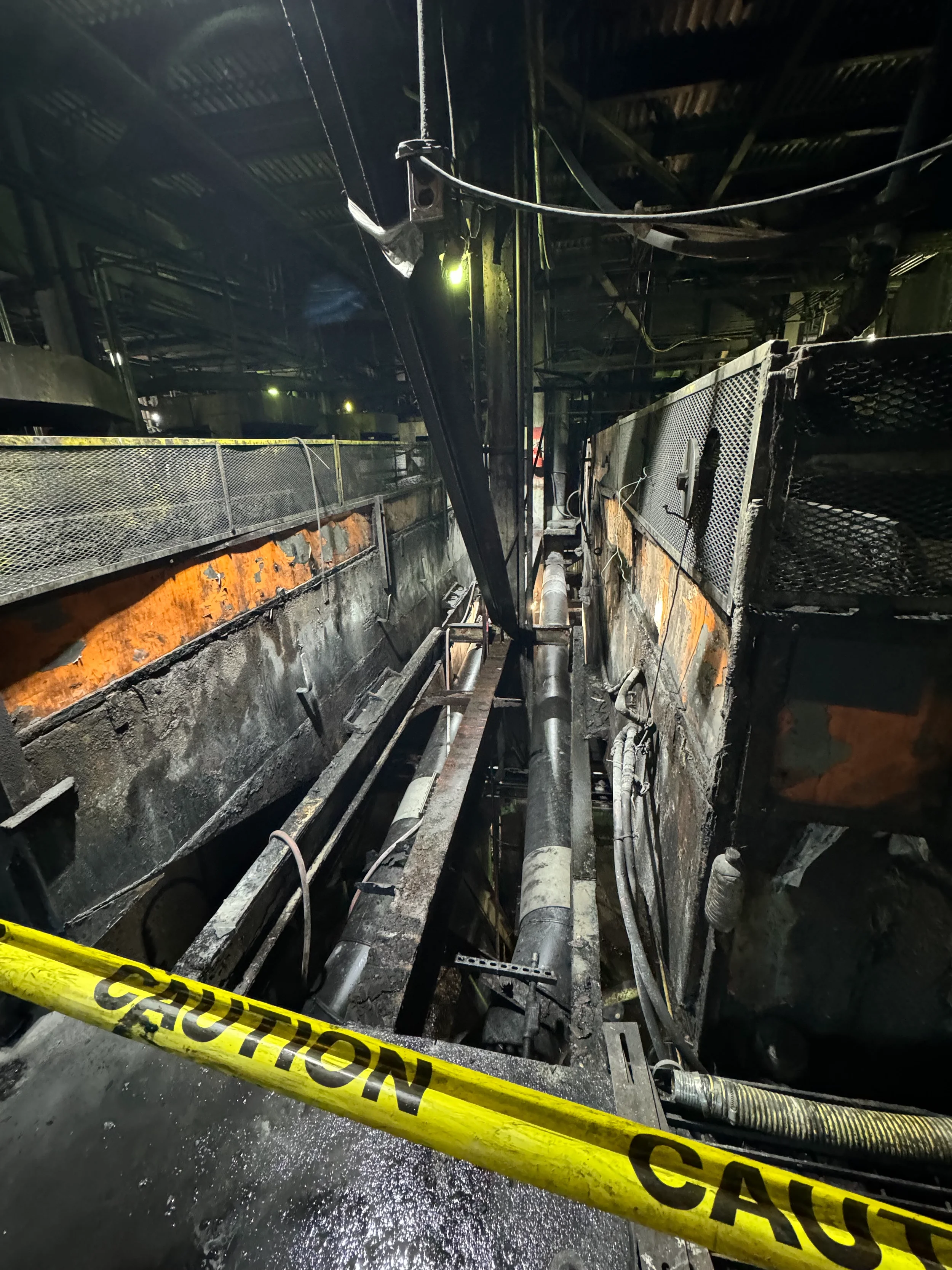 Fire-damaged industrial or commercial building interior, with charred walls, burnt equipment, and caution tape in the foreground.