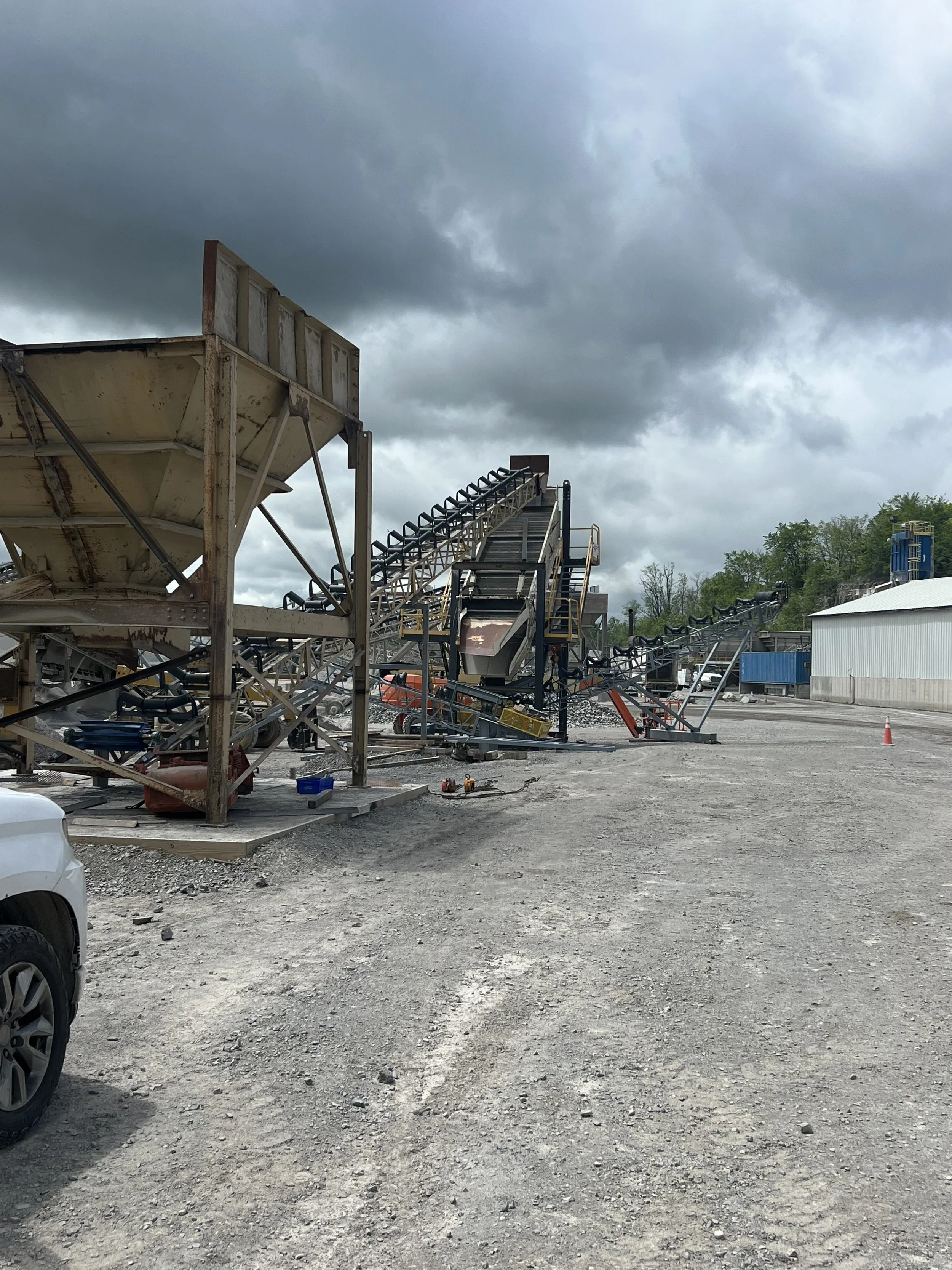 View of an industrial or construction site with conveyor belts, metal structures, and equipment under a cloudy sky.