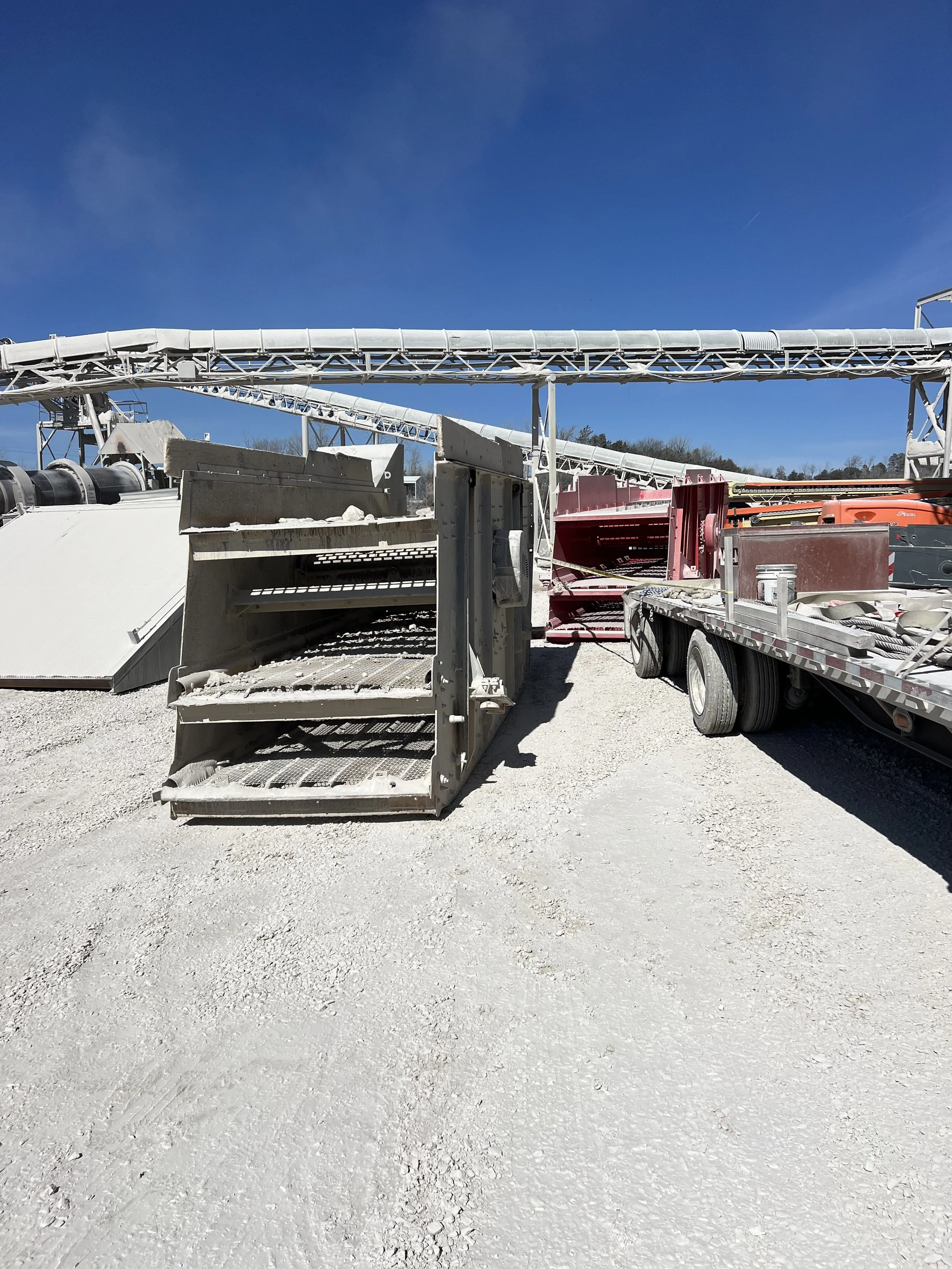 Construction site with large white conveyor system and equipment on a gravel surface under a clear blue sky.