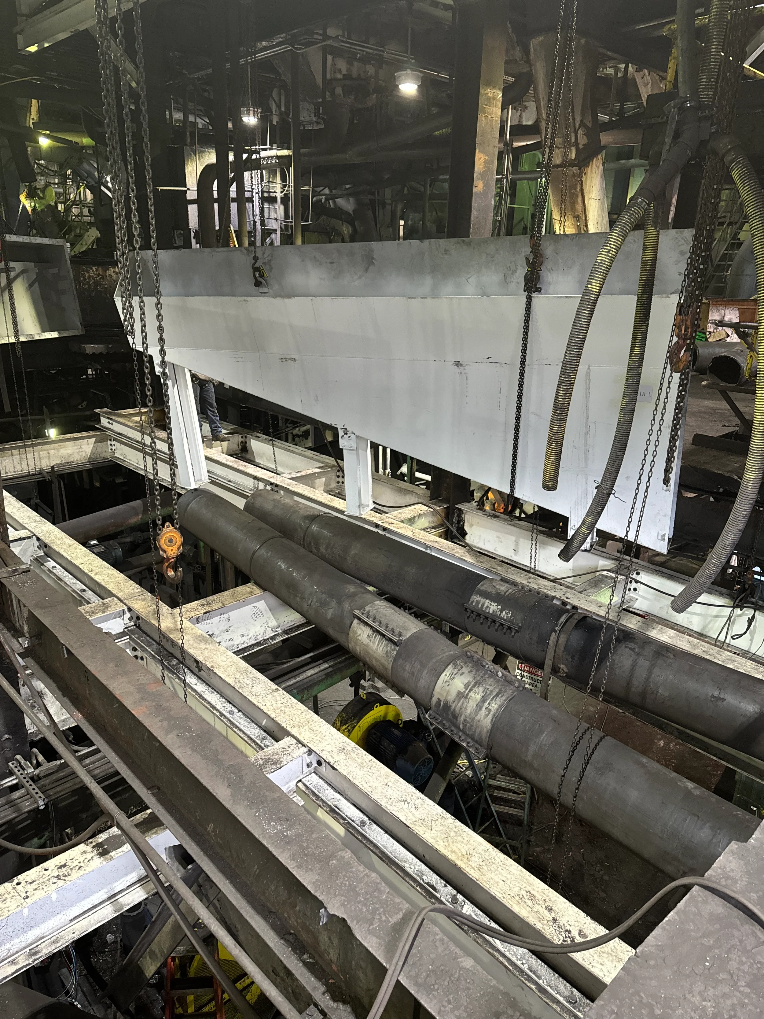 Industrial construction site with metal beams, pipes, chains, and construction equipment, under dim lighting.