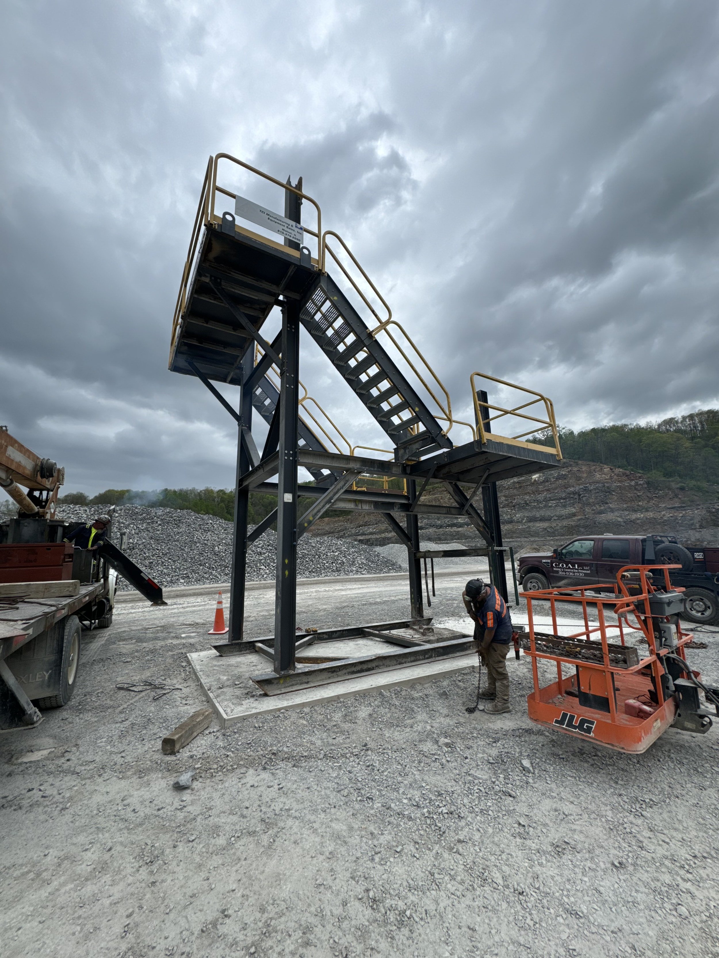 Construction worker installing a large staircase on a gravel site with cloudy sky overhead.