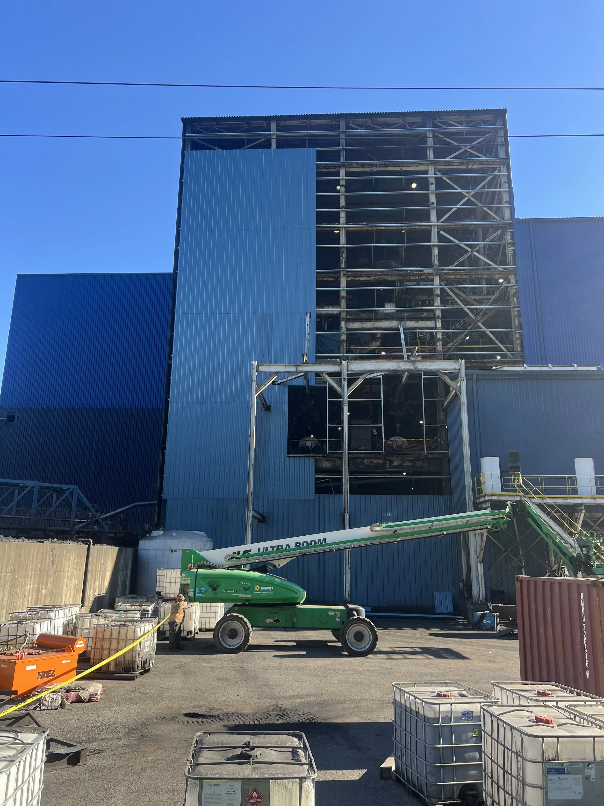 Construction site with a partially built multi-story building, construction equipment, and materials in the foreground, under a clear blue sky.