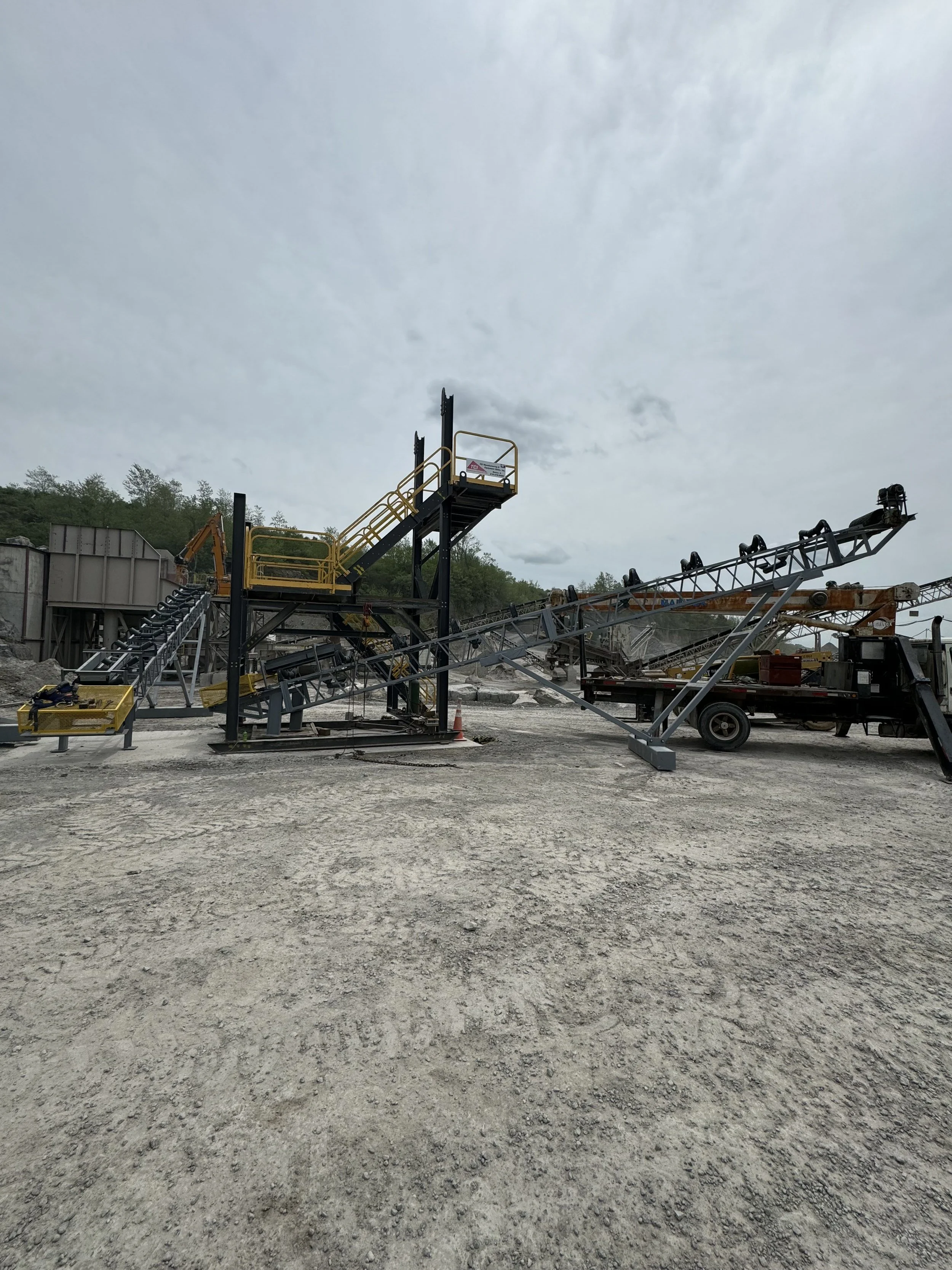 An outdoor construction site with conveyor belts and machinery under a cloudy sky.