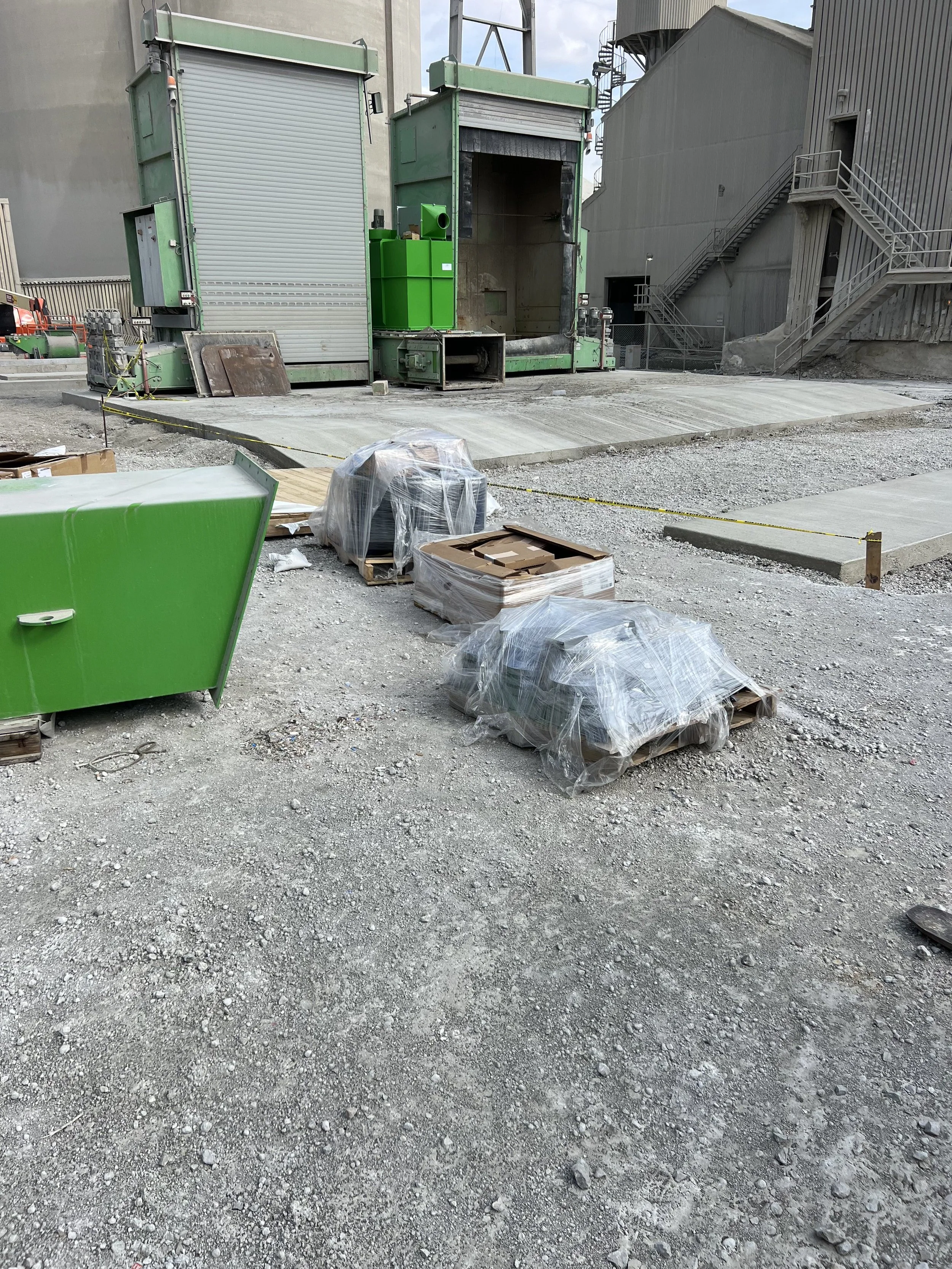 Construction site with gravel ground, green equipment, and concrete pavement in progress.