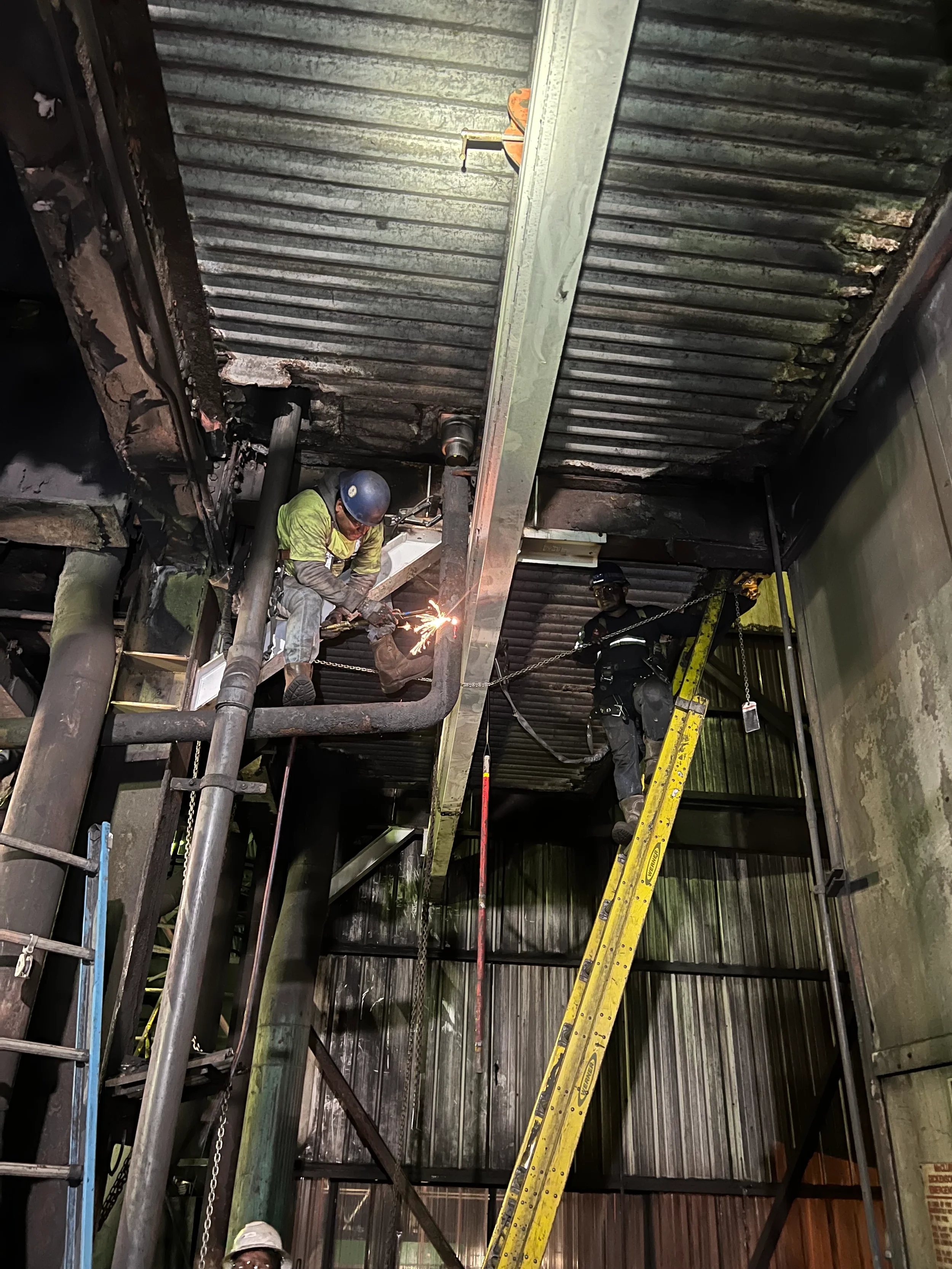 Workers welding and inspecting steel beams inside an industrial building under construction.