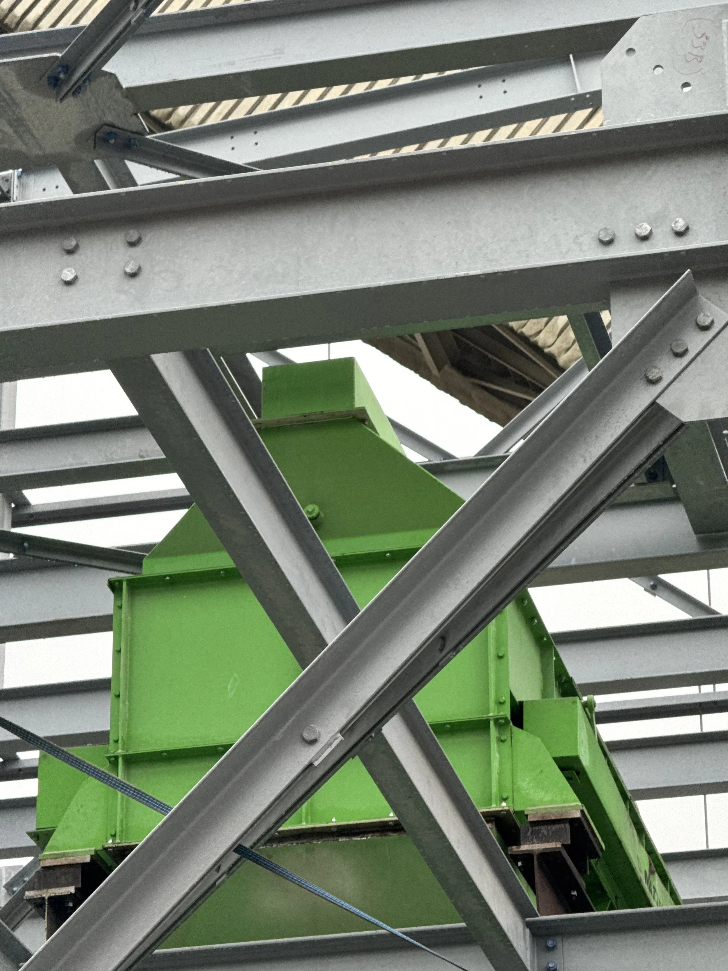 Metal framework of an industrial staircase with green supports and diagonal beams in a factory or warehouse.
