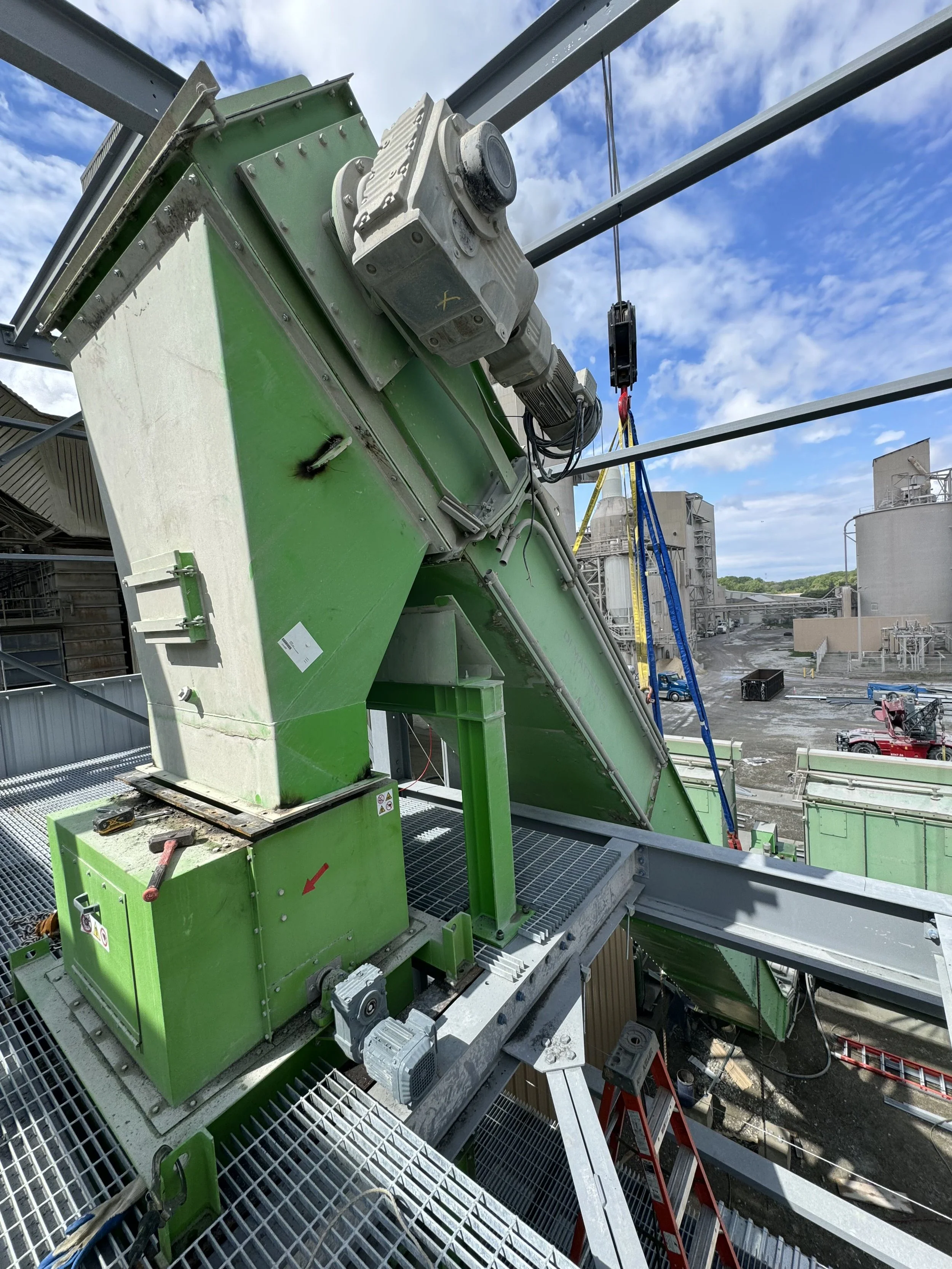 Construction site with green machinery and scaffolding under blue sky with clouds.