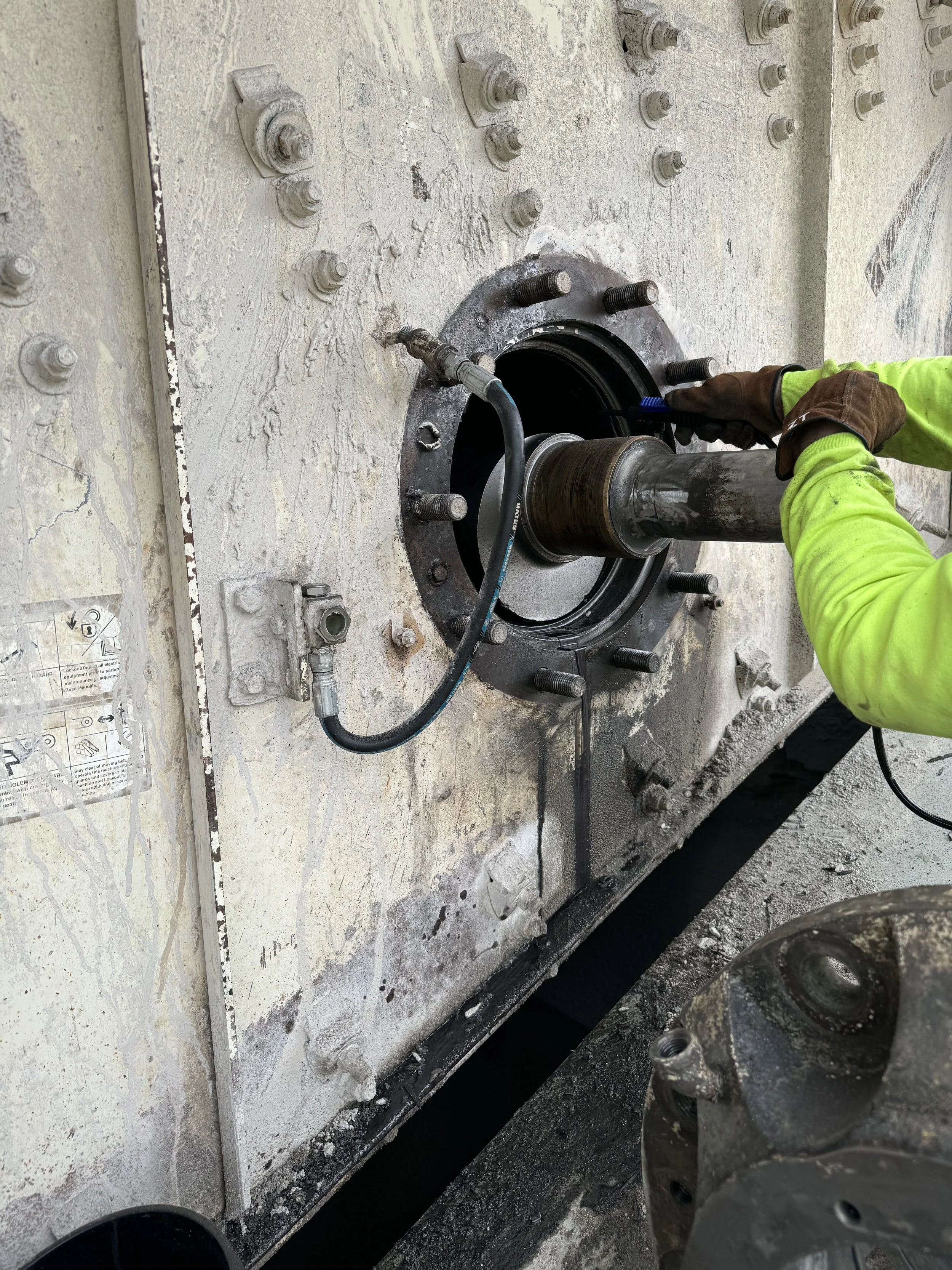 Worker installing or repairing a large industrial pipe flange on a concrete wall, using a tool to secure the connection.