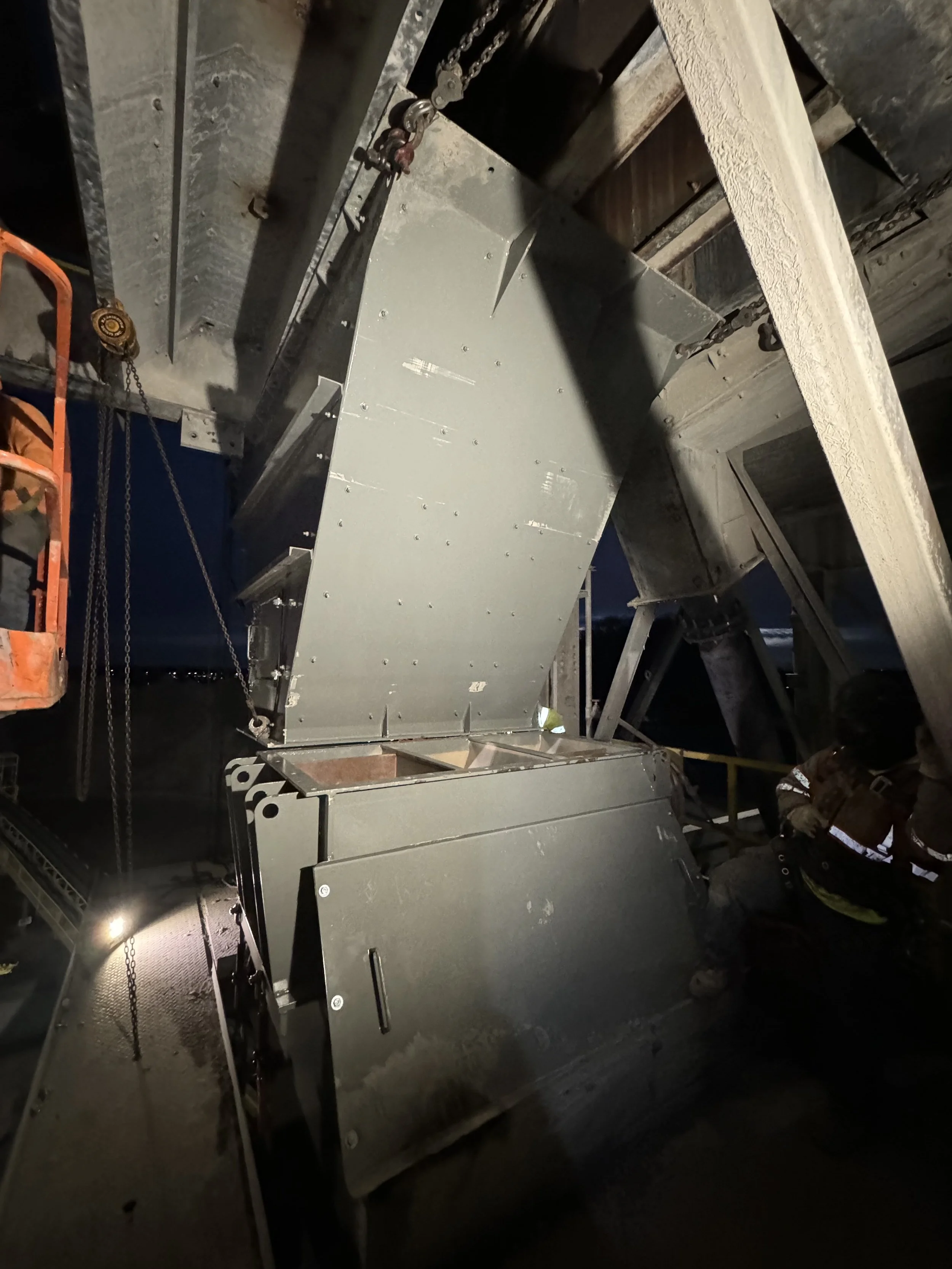 Construction worker working with metal panels on a ceiling, scaffolding and chains visible in a dark industrial setting.