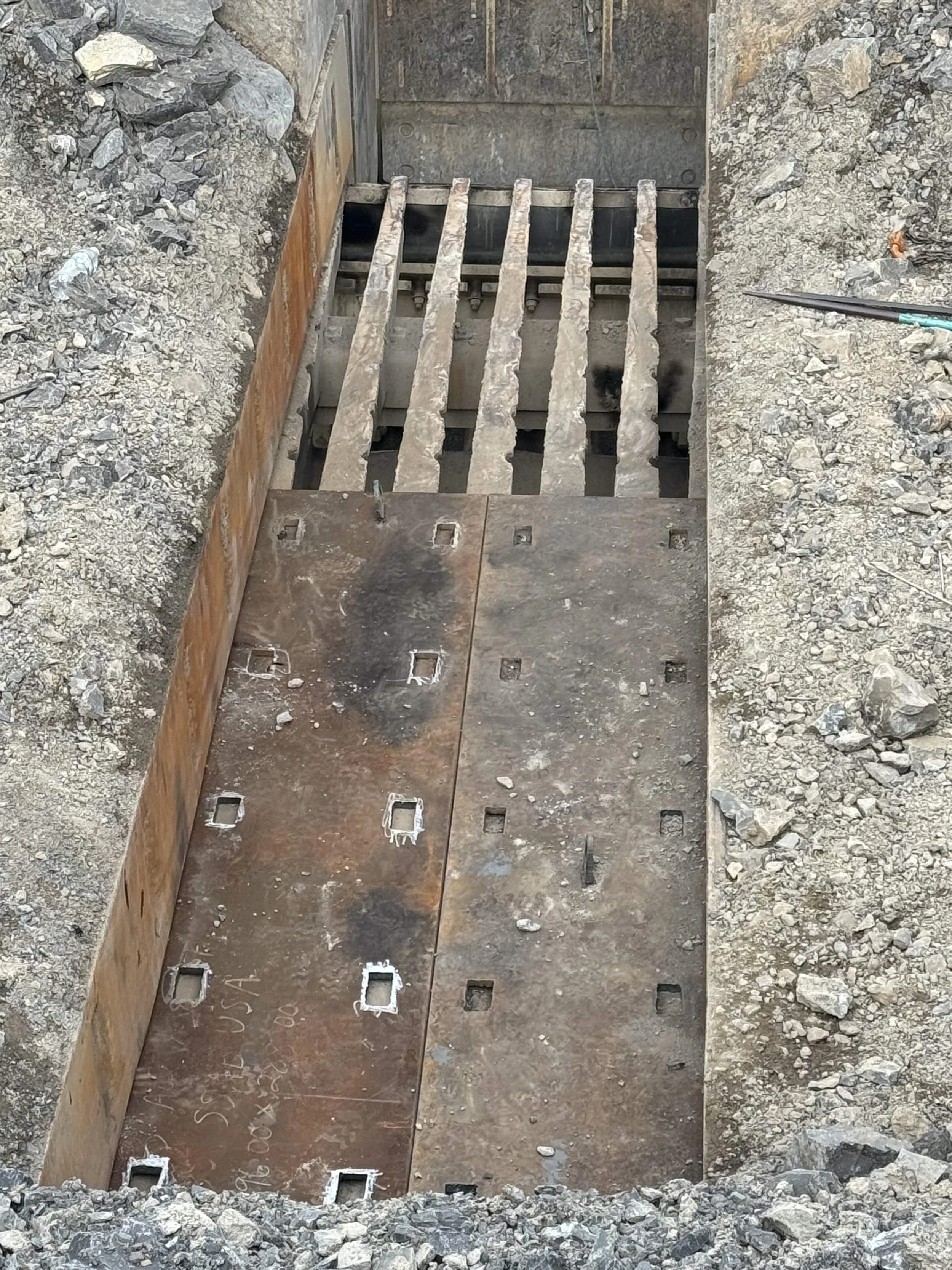 Construction site showing a deep excavated hole with steel reinforcement and wooden formwork for concrete construction.