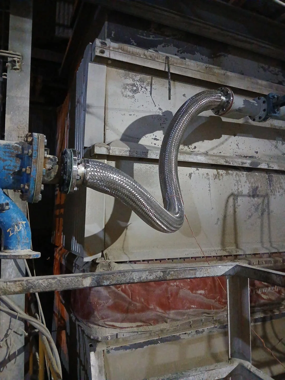 Industrial piping with flexible metallic hoses connected to a pipeline in a workshop or factory setting.