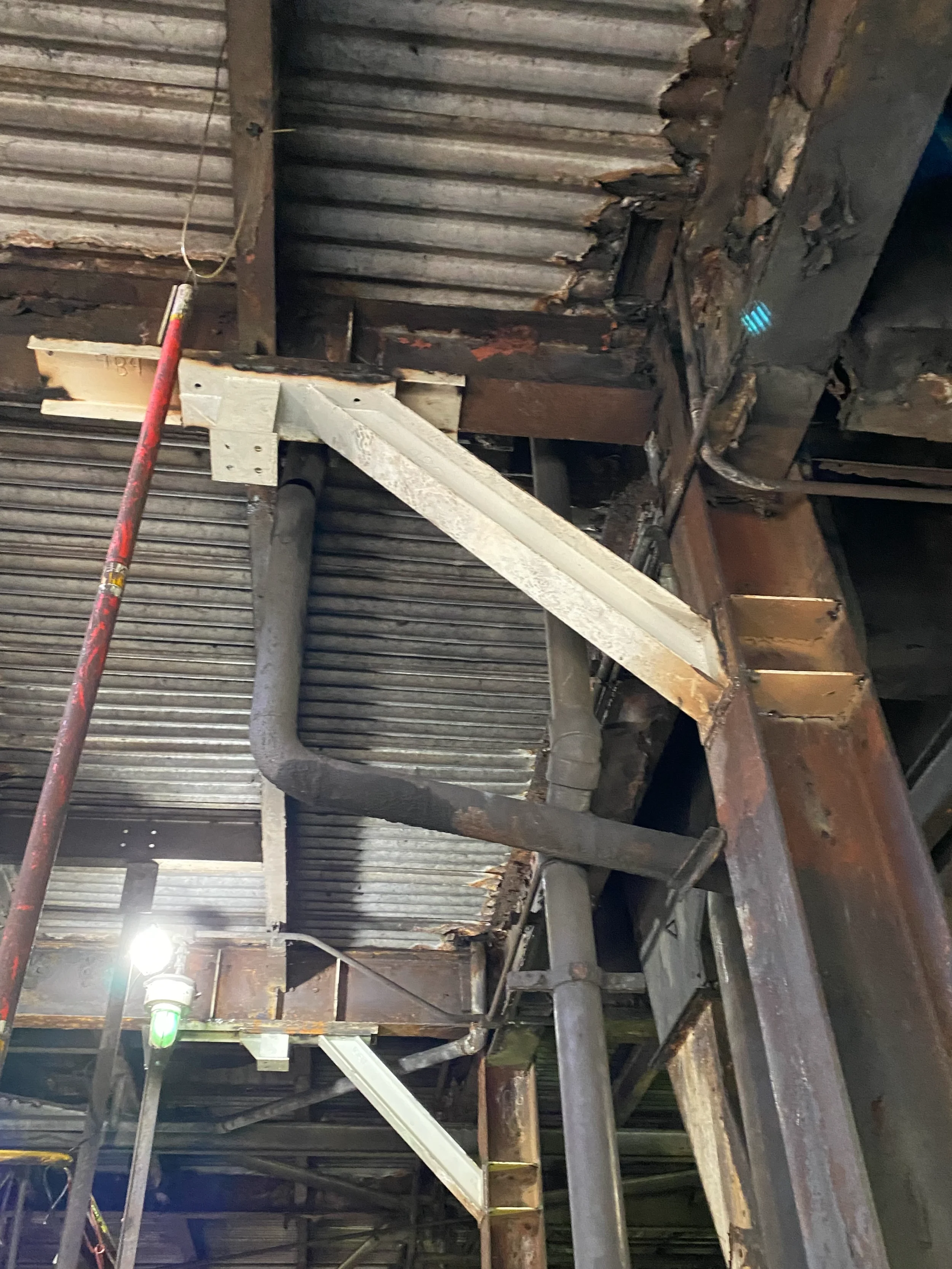 Interior of an industrial building with rusted metal and pipes, and a bright green light at the bottom left.