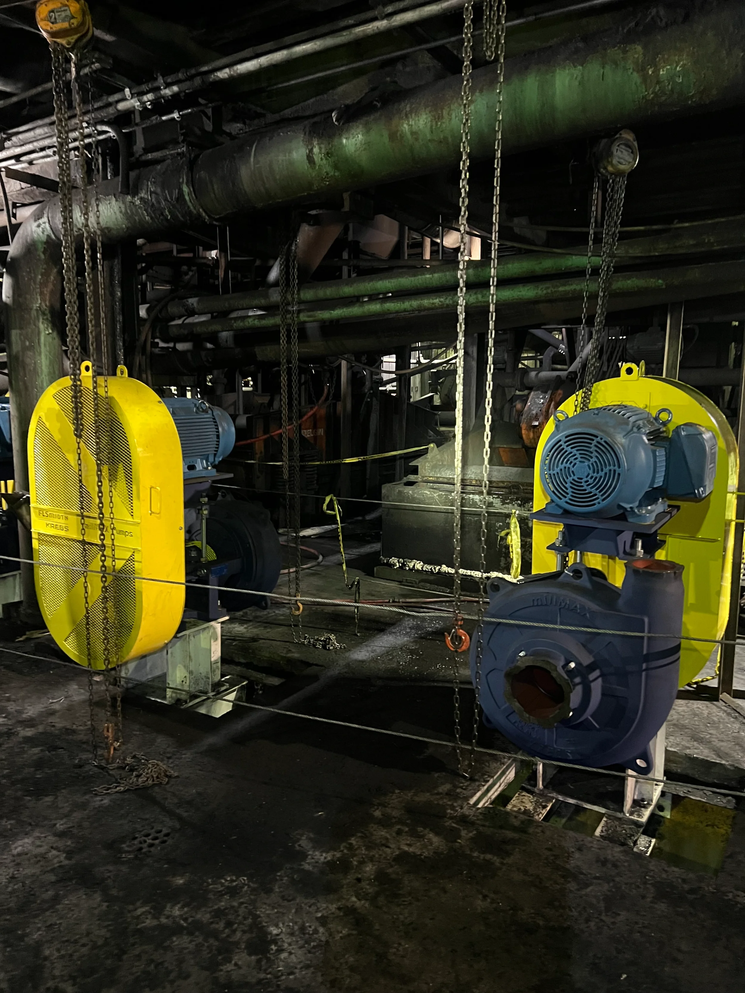 Industrial machinery and electrical equipment inside a dark facility, with pipes, motors, and safety barriers.