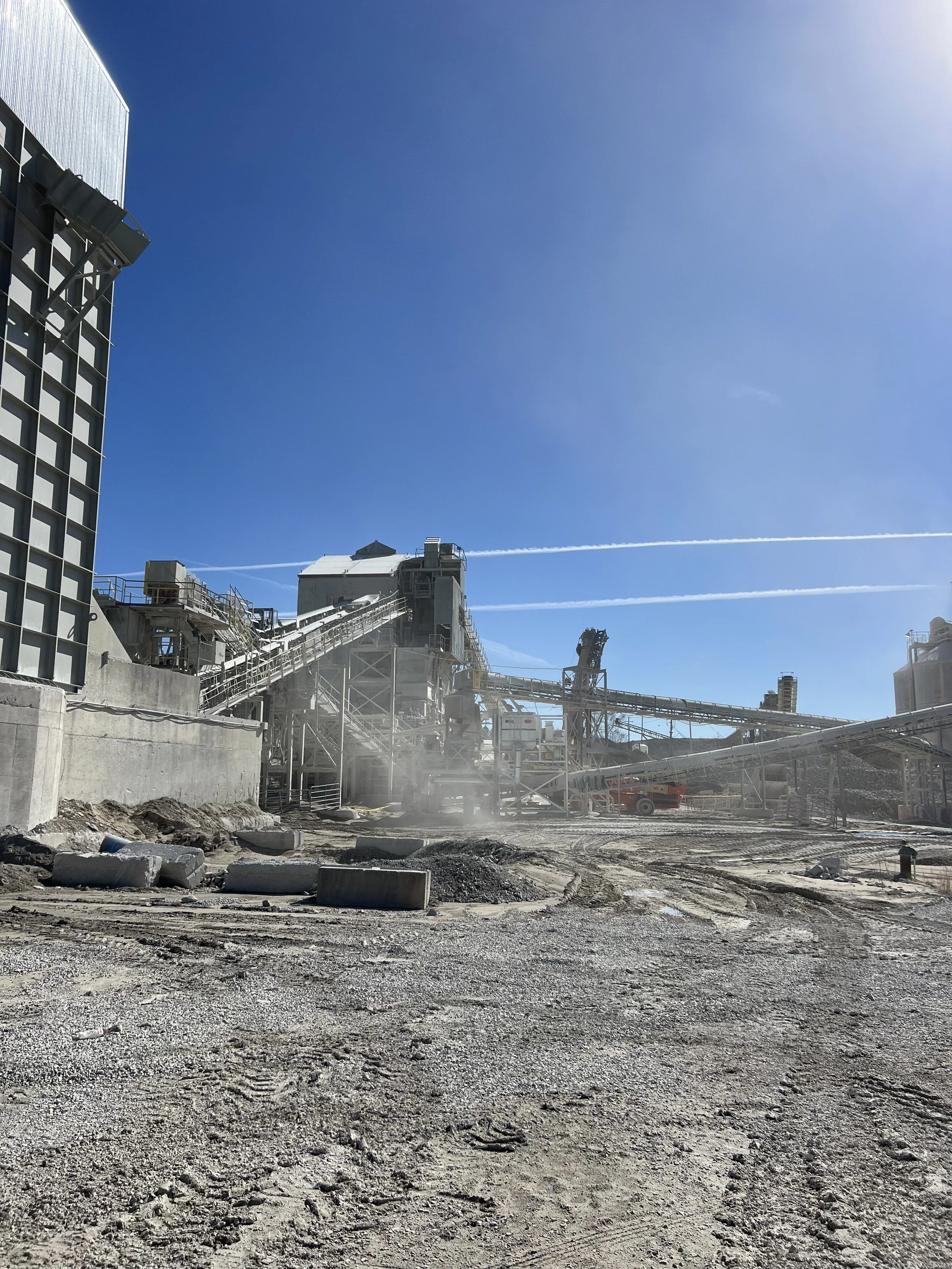 Construction site with industrial buildings, pipelines, and machinery under a clear blue sky.