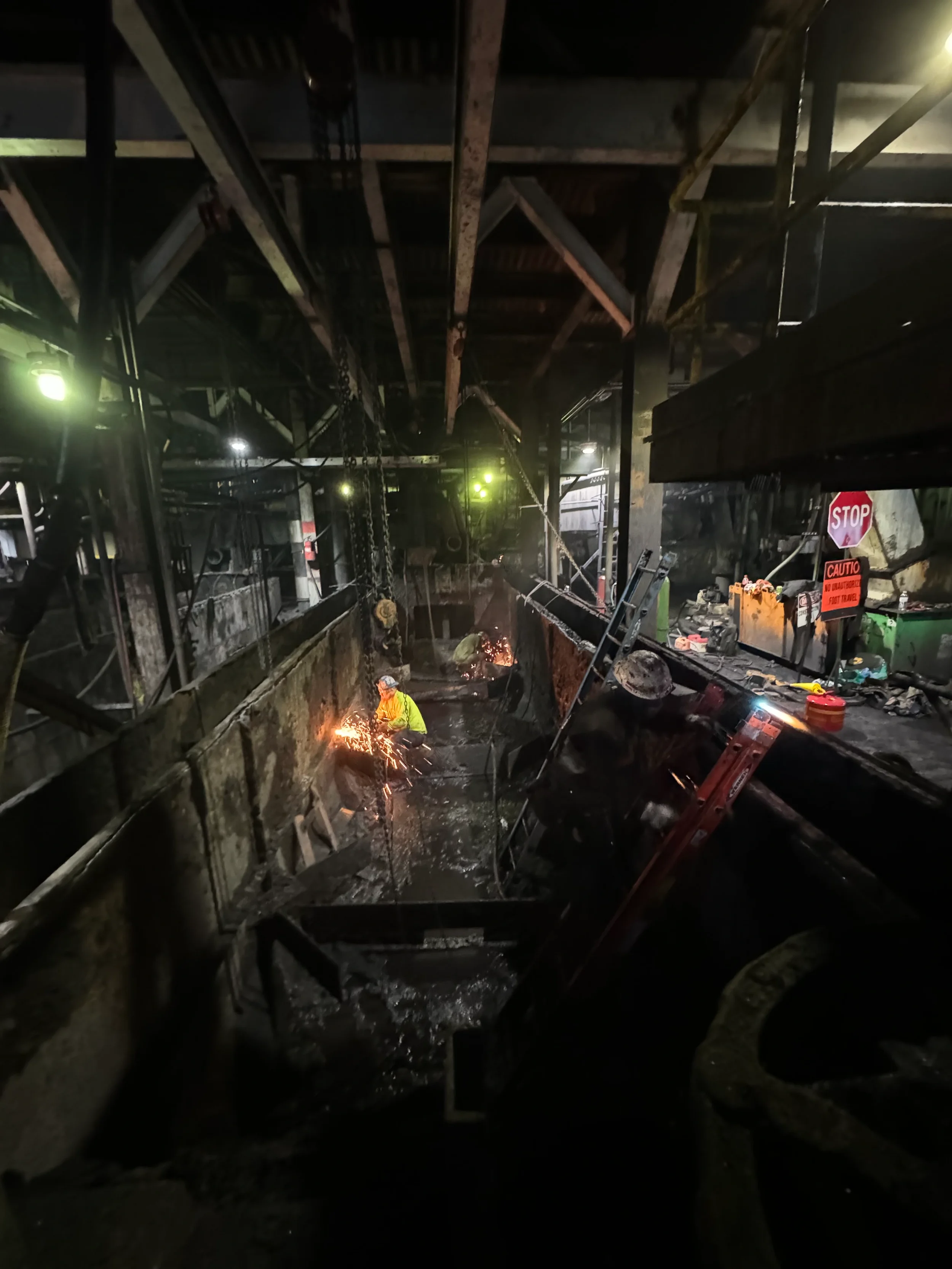 Worker welding inside a dark industrial construction site with parts of the ceiling and structure visible, illuminated by sparks from welding.