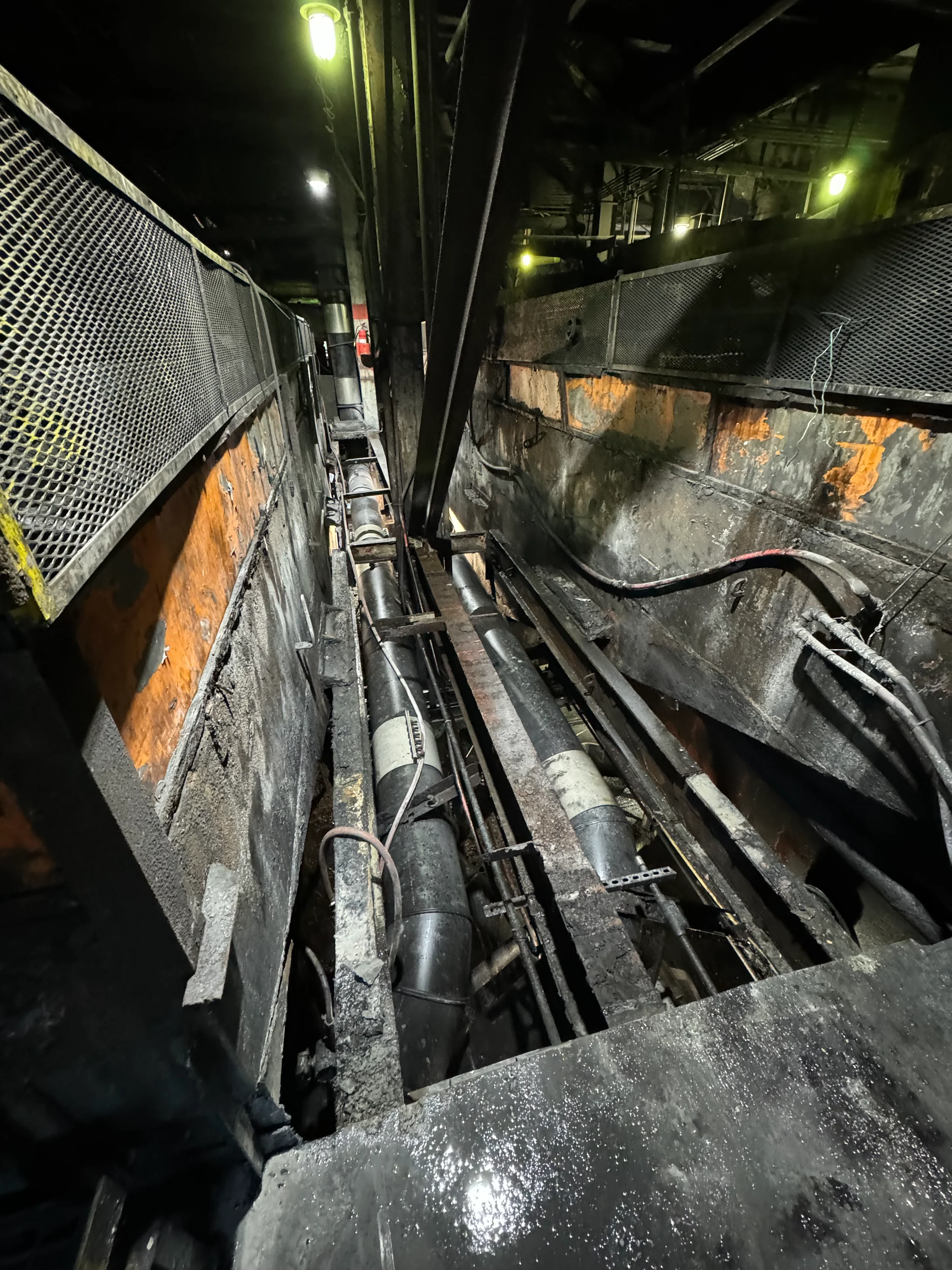 Industrial scene showing machinery, pipes, and railings in a dark, gritty environment, possibly a factory or construction site.