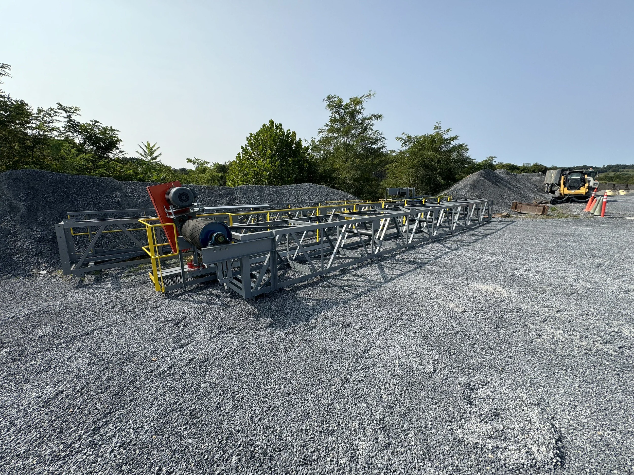 Construction site with gravel, machinery, and safety cones under a clear blue sky.