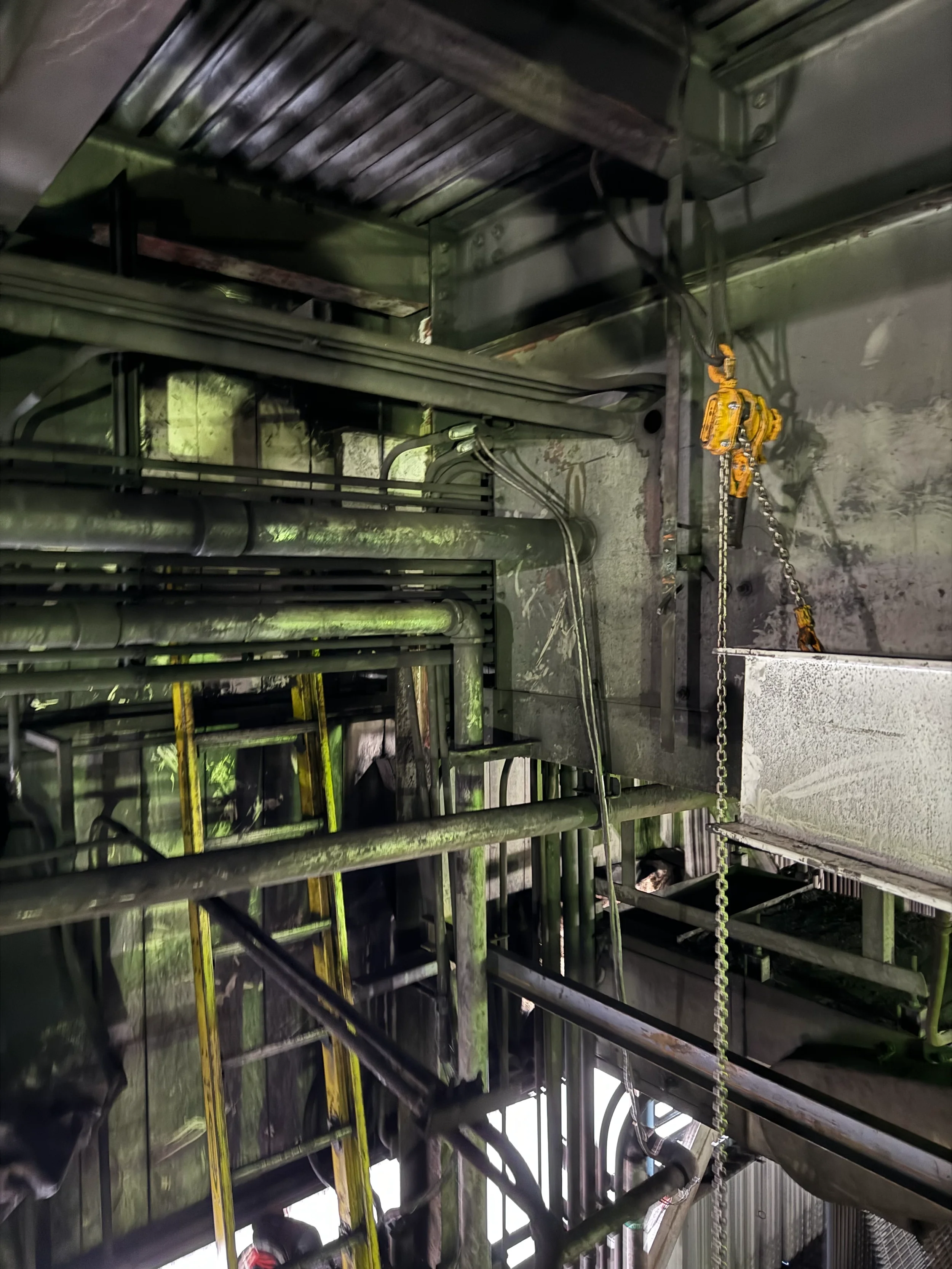 Industrial piping system with metal pipes, ladders, and safety chains in a factory or plant setting.