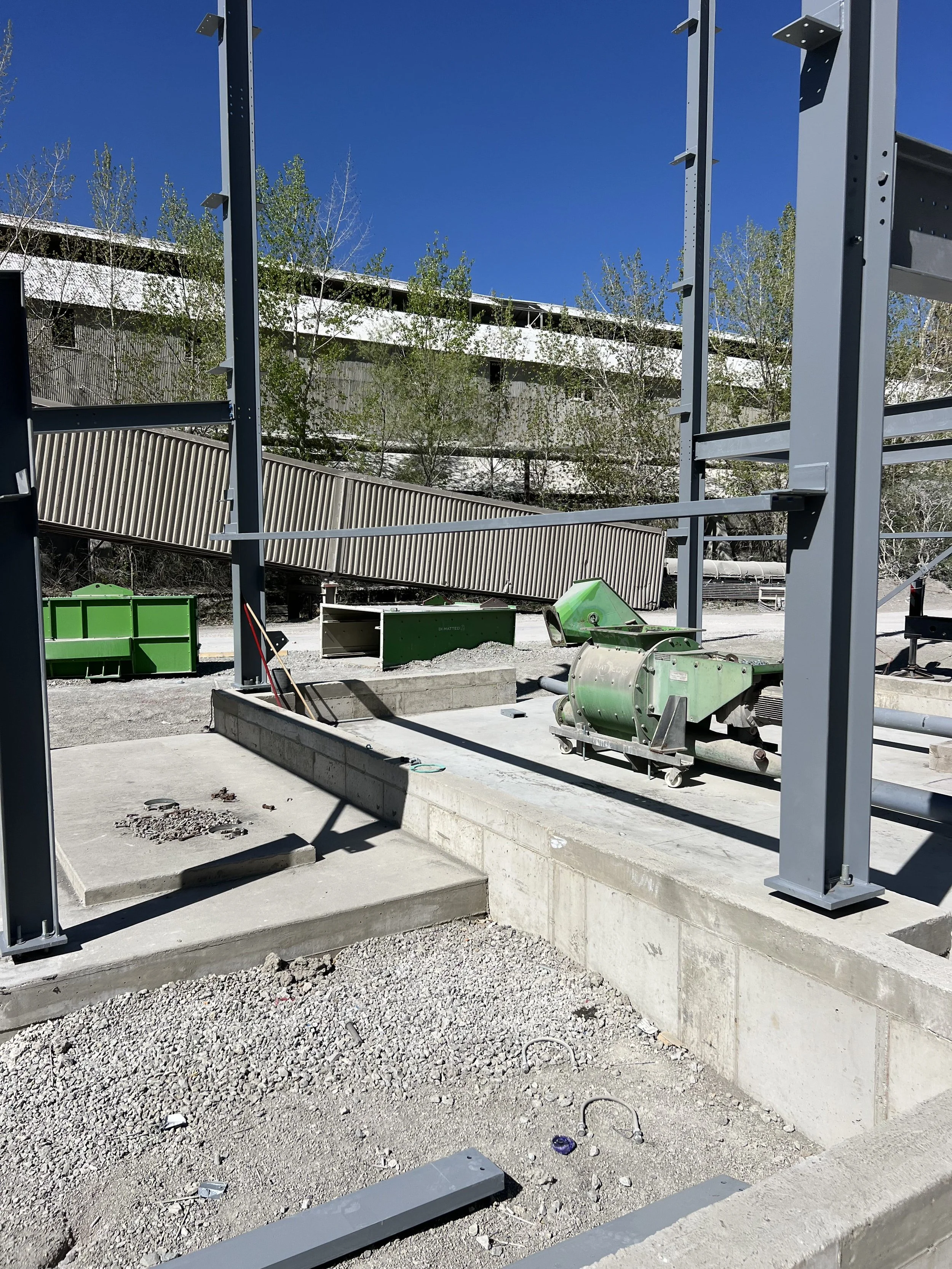 Construction site with metal framework, gravel ground, and scattered construction materials under a clear blue sky.
