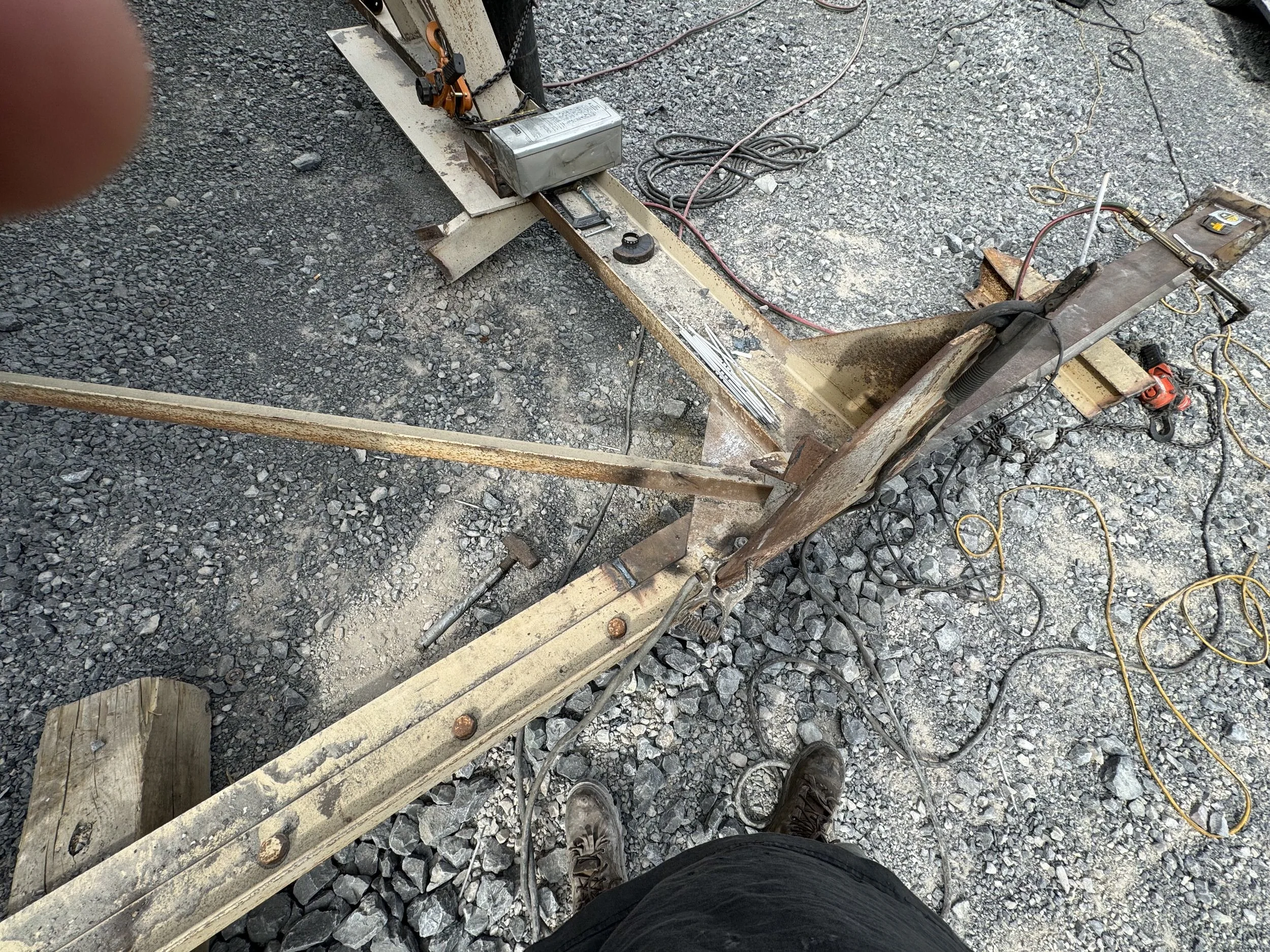 View from a construction worker looking down at the ground, showing gravel, wooden beams, and various construction tools and wires on a construction site.