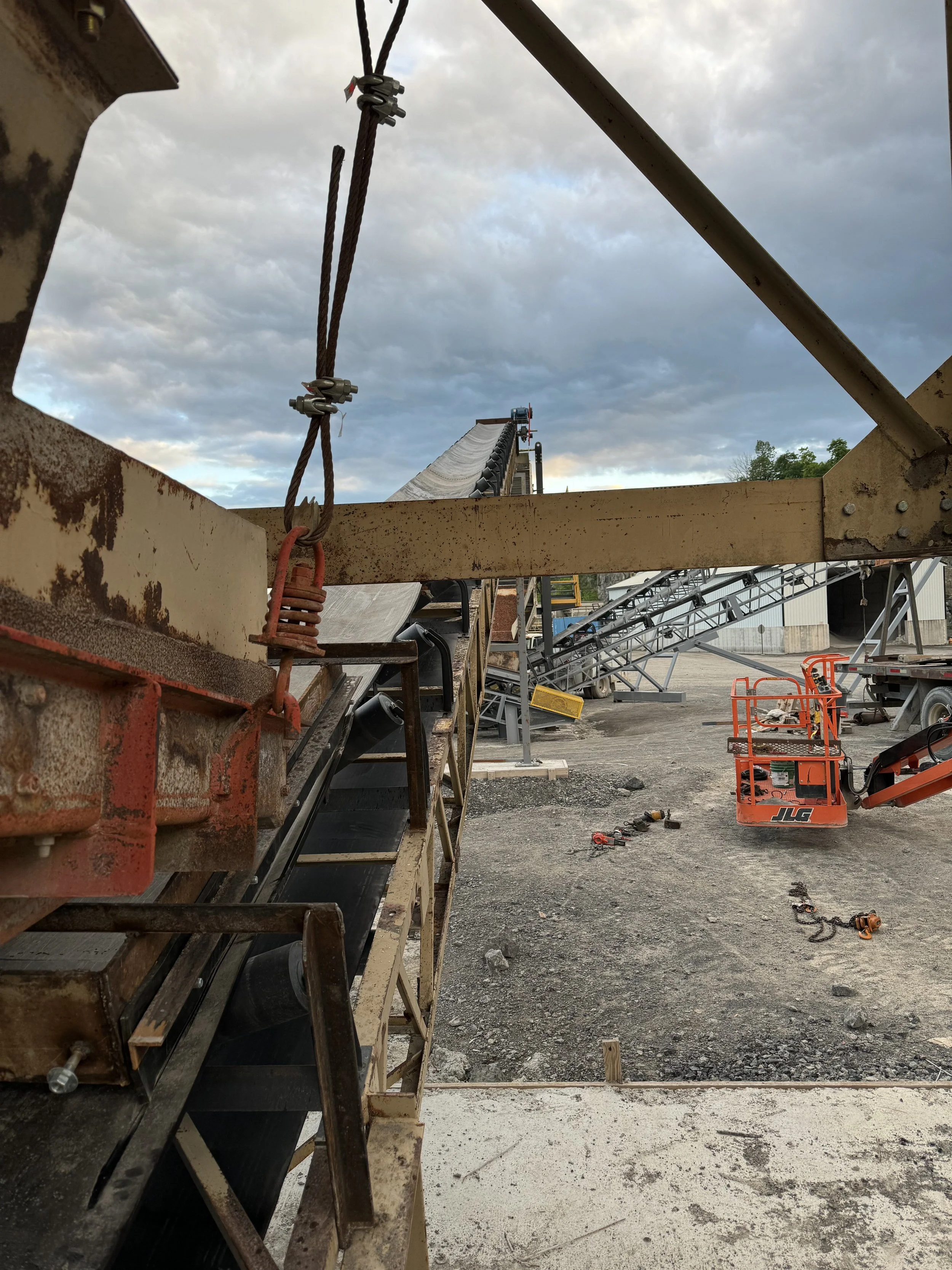 View of a construction site with metal framework, tools, equipment, and equipment carts, under a cloudy sky.