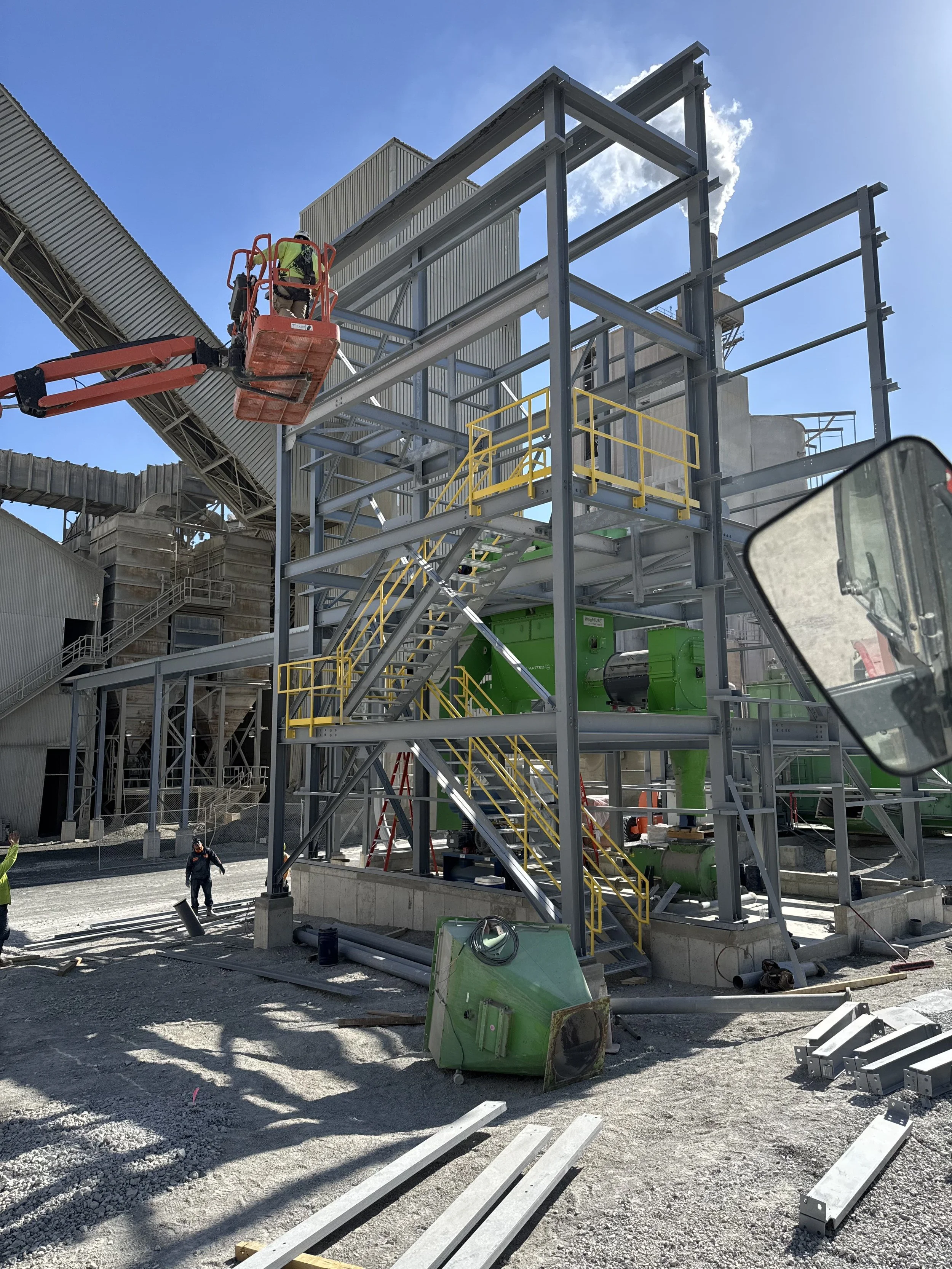 Construction site with steel framework, yellow stairs, workers, and equipment, under a clear blue sky.