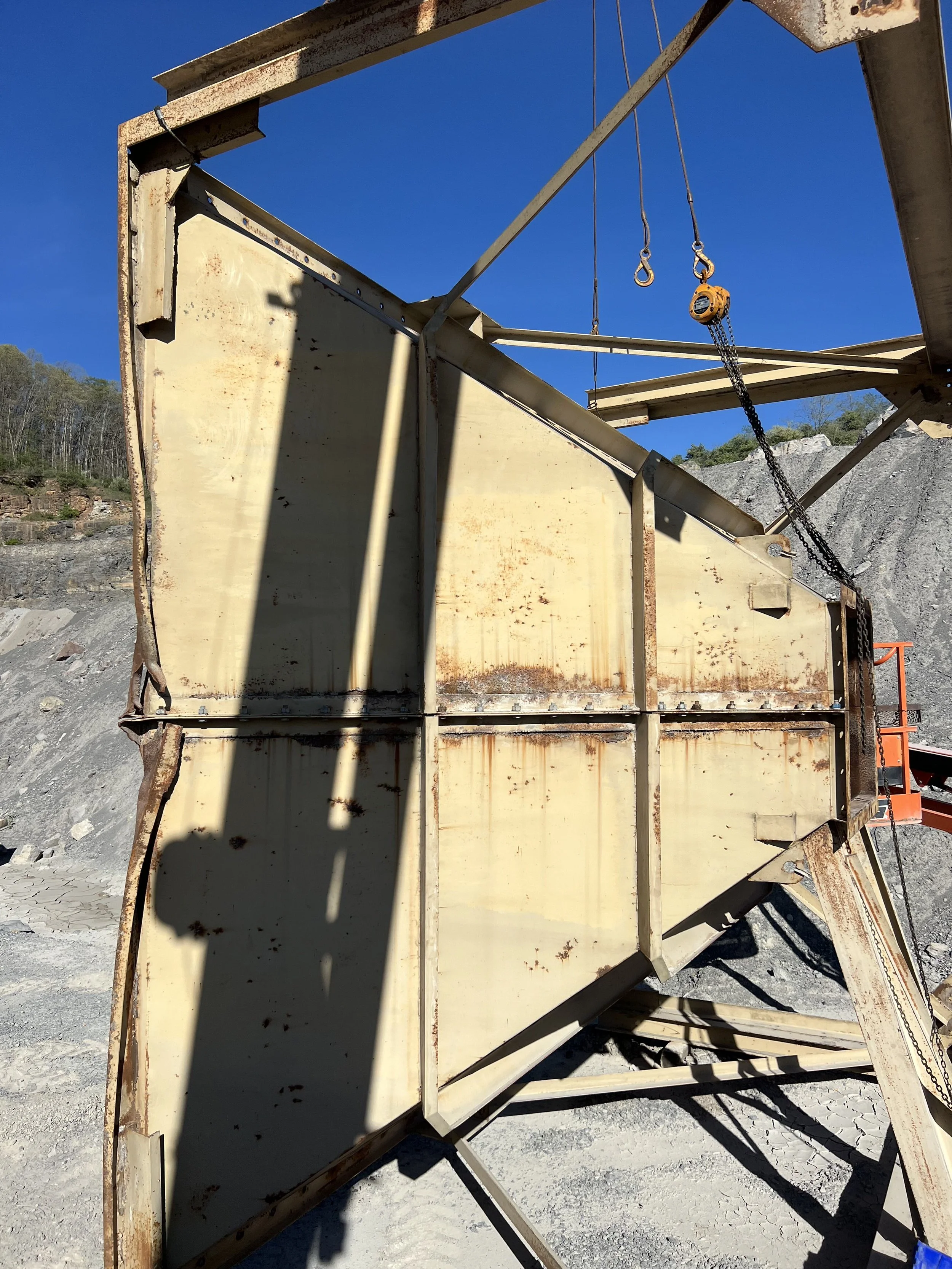 A rusty construction platform or scaffold with chains and pulleys in an outdoor area with rocky terrain and clear blue sky.