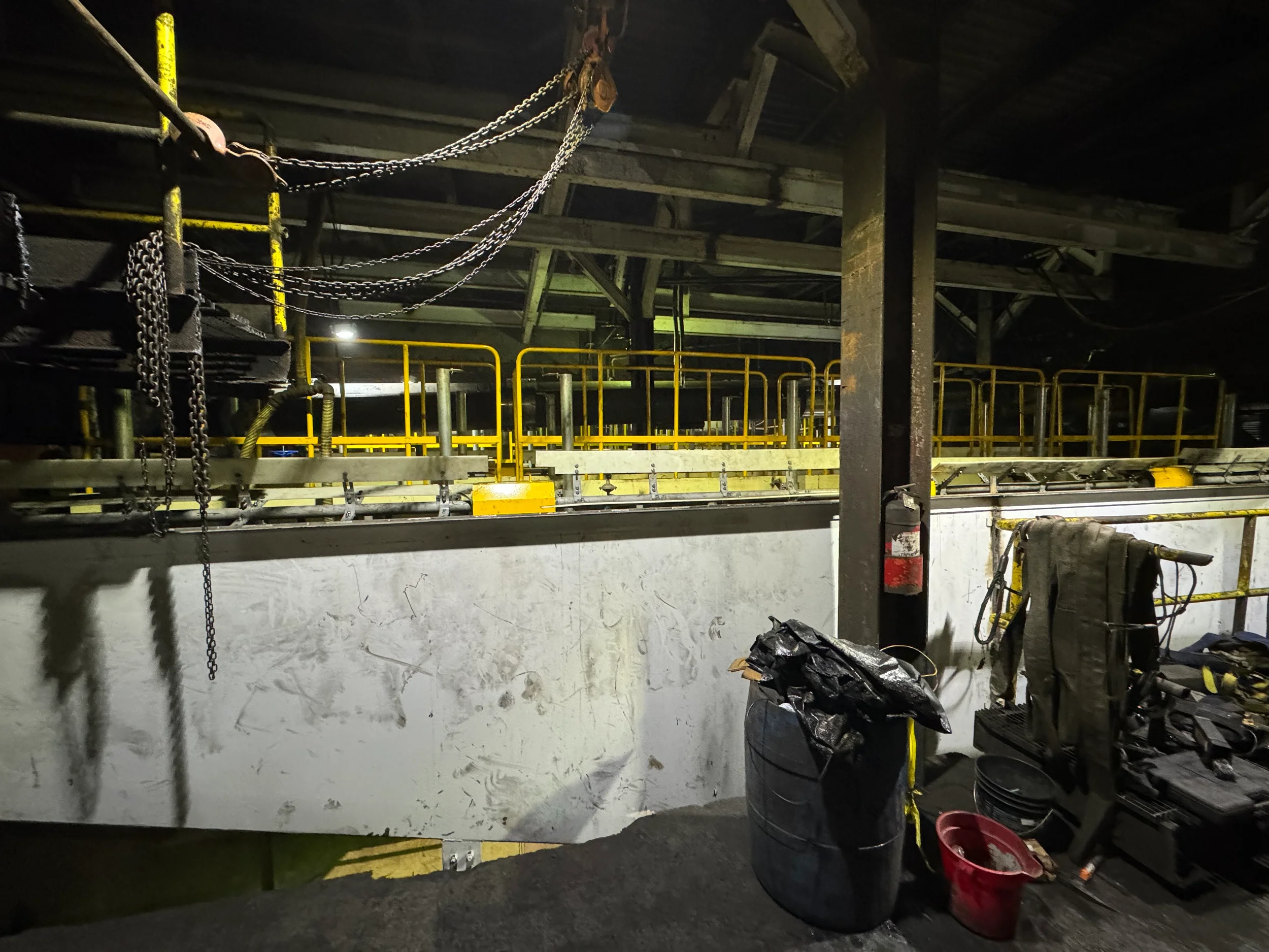 Underground construction site with scaffolding, safety chains, and construction tools. Dimly lit with yellow safety railings and various equipment, indicating ongoing infrastructure work.