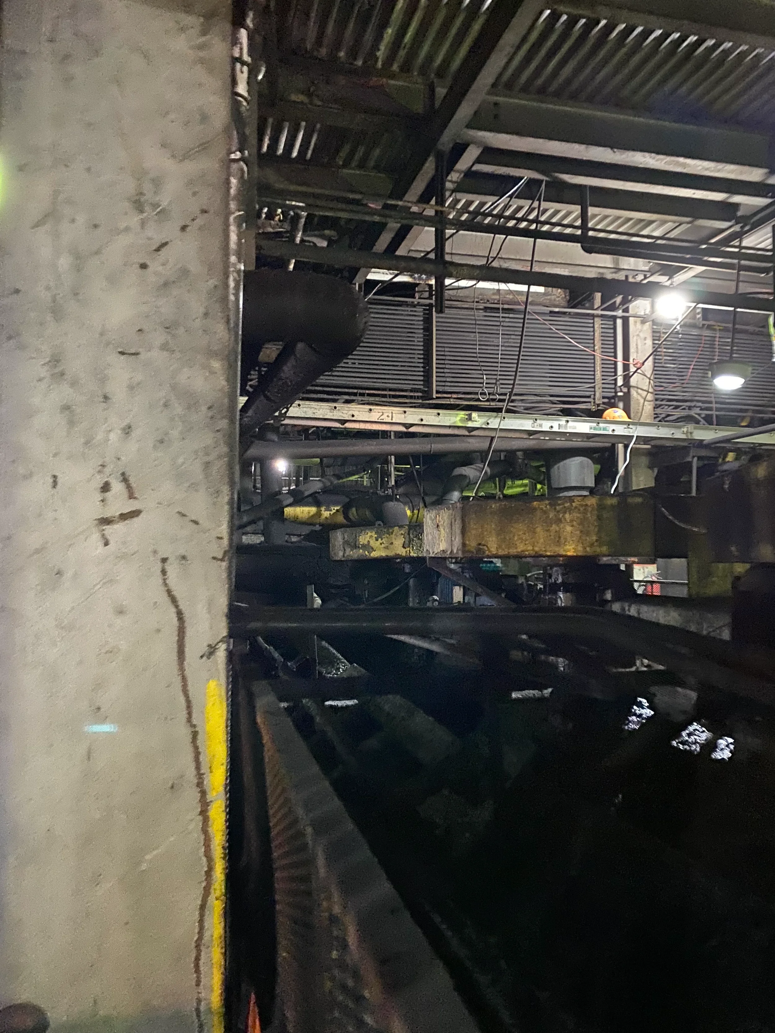 Construction site with metal scaffolding, pipes, and a concrete floor, illuminated by brightness on the right side.