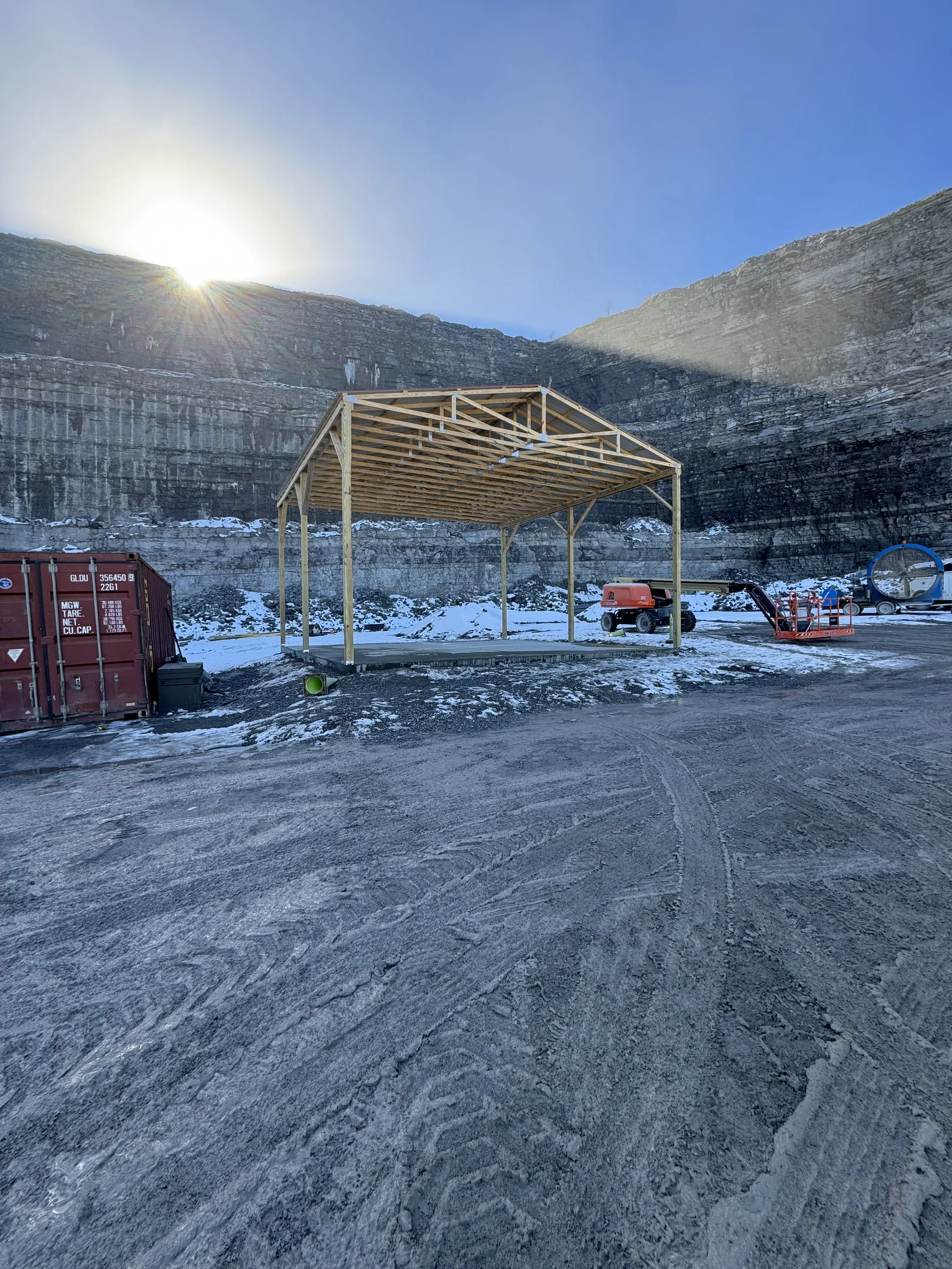 Construction site in a snowy mountainous area with a wooden framework and construction equipment.