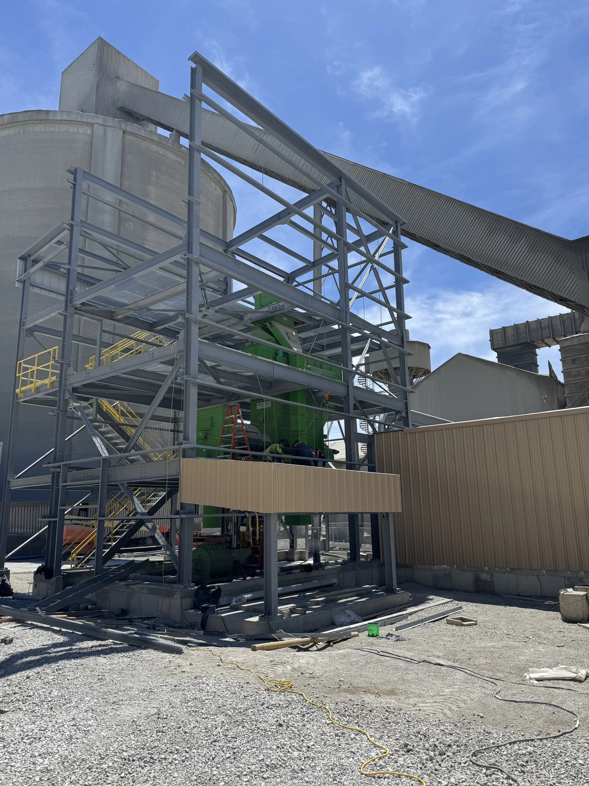 Construction site with metal framework and green industrial equipment, outdoor setting under a clear blue sky.