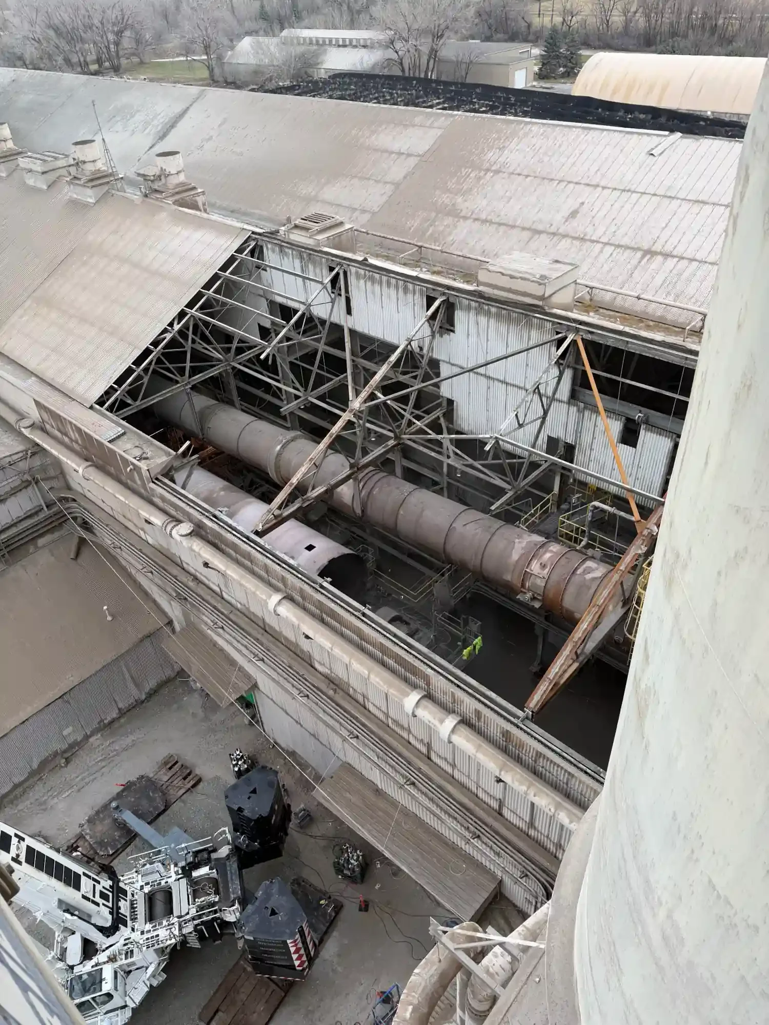 View from a high-rise building showing a damaged industrial rooftop with collapsed metal structures, scattered equipment, and a fire truck below.