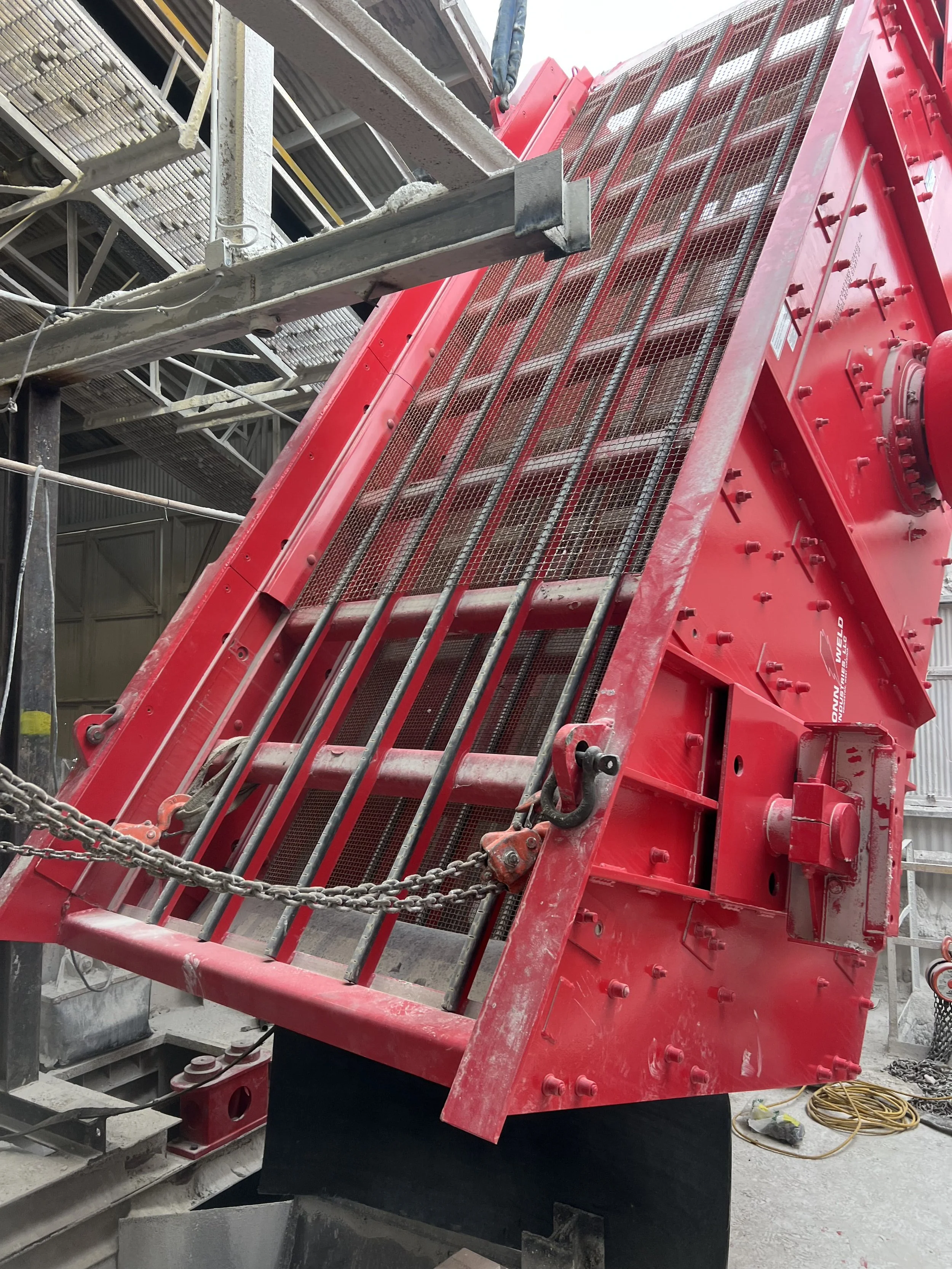 Close-up of a large red industrial machine at a construction site, with metal bars, chains, and bolts visible.