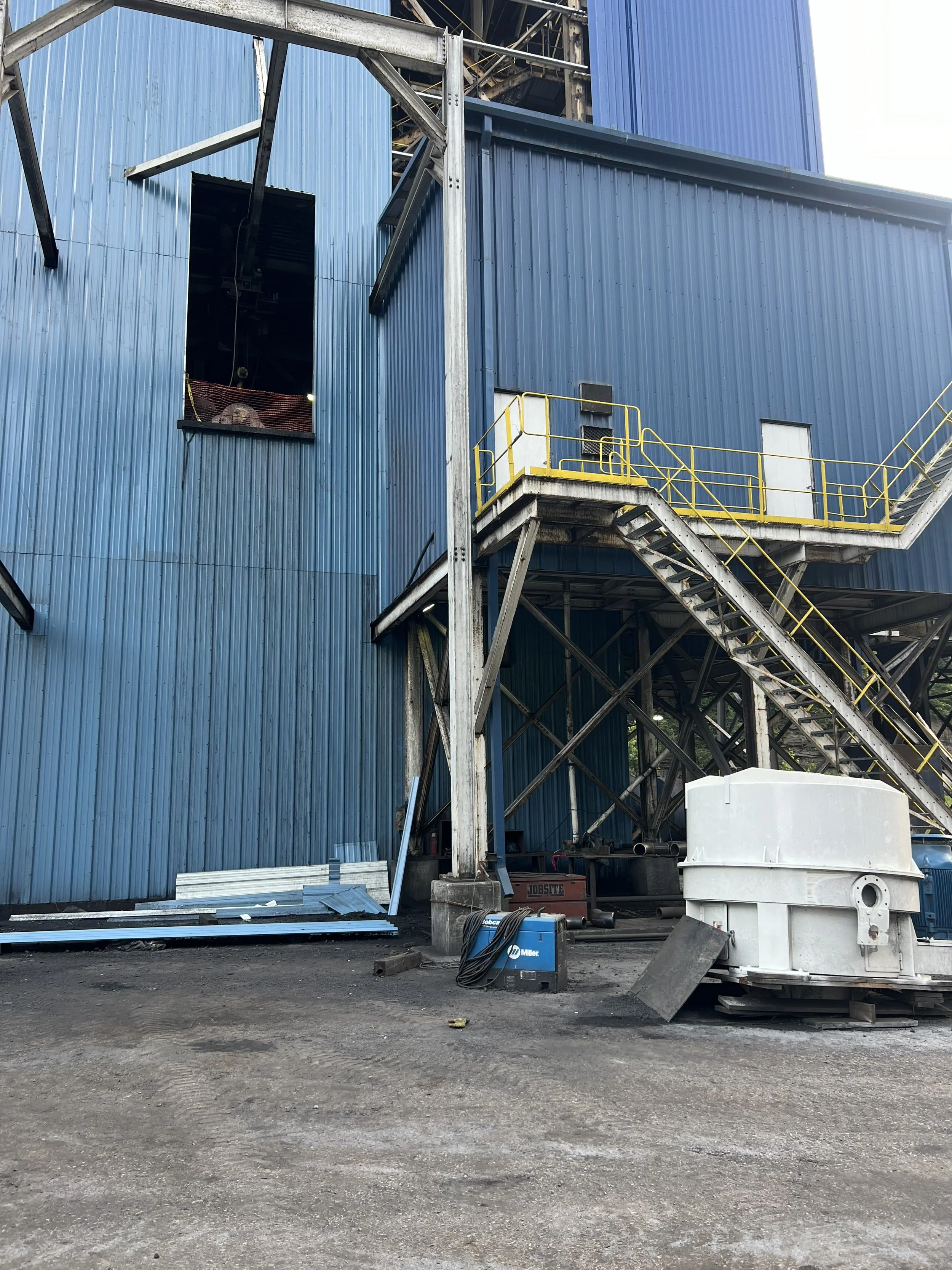 Construction site with a blue metal building, metal stairs, and construction equipment.