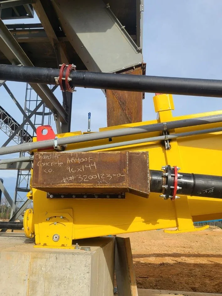 Close-up of industrial piping and equipment, including black pipes, a yellow structure, and a brown steel block with handwritten notes. Part of a construction or industrial site.